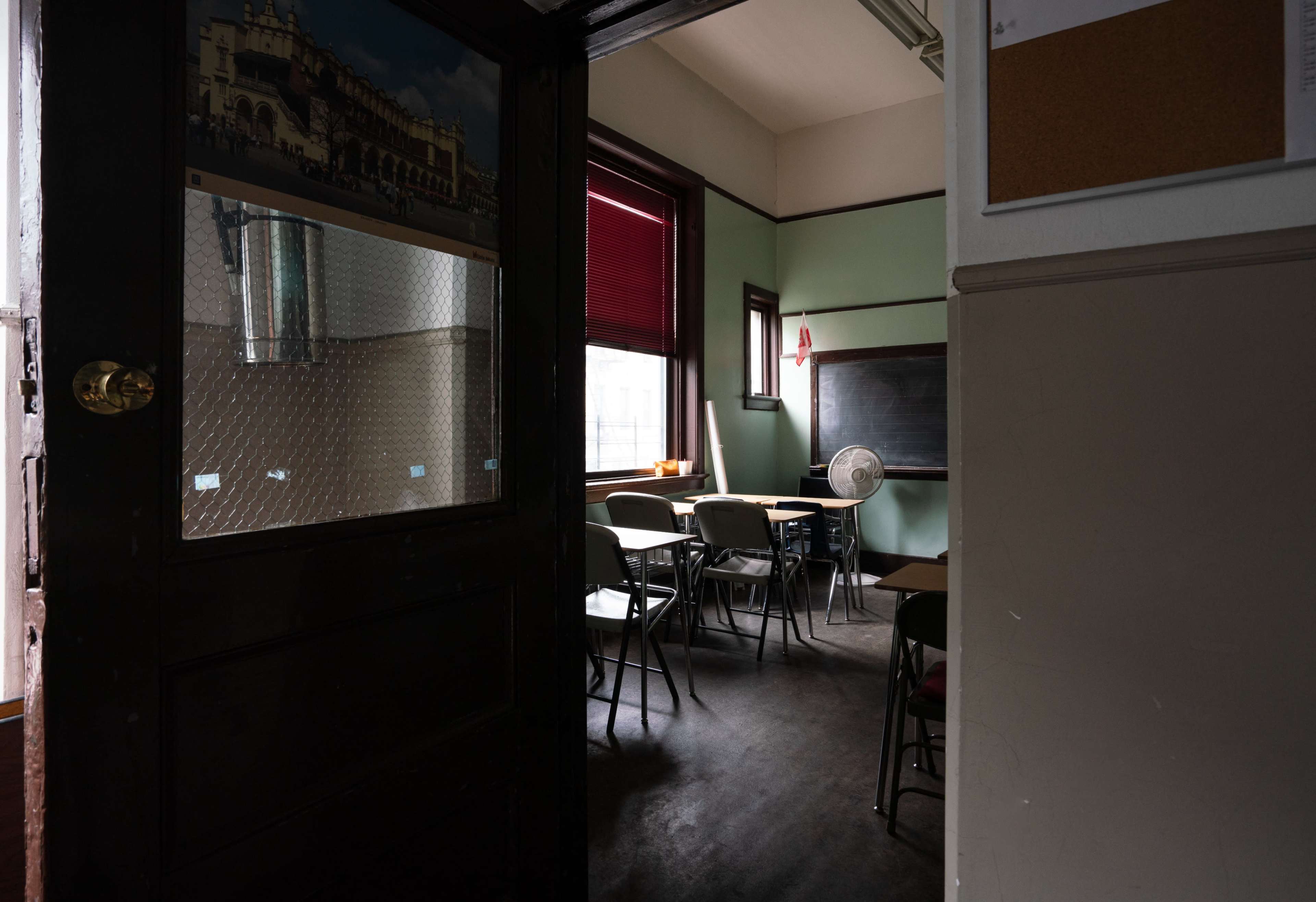 A portion of a classroom is visible through an open door, showing empty desks and a chalkboard against a green wall.
