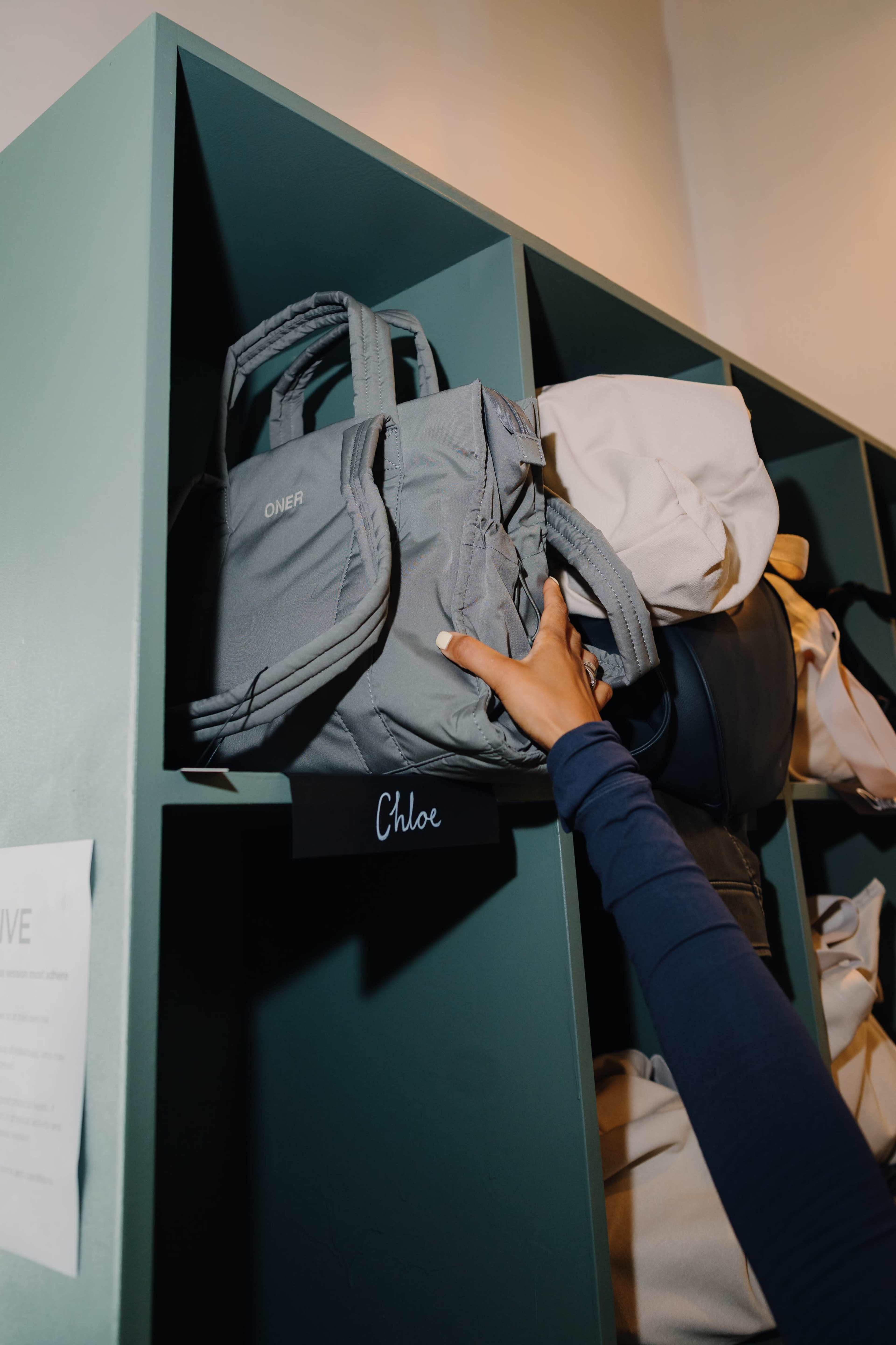 A person is reaching for a gray bag on a shelf labeled with the name "Chloe."