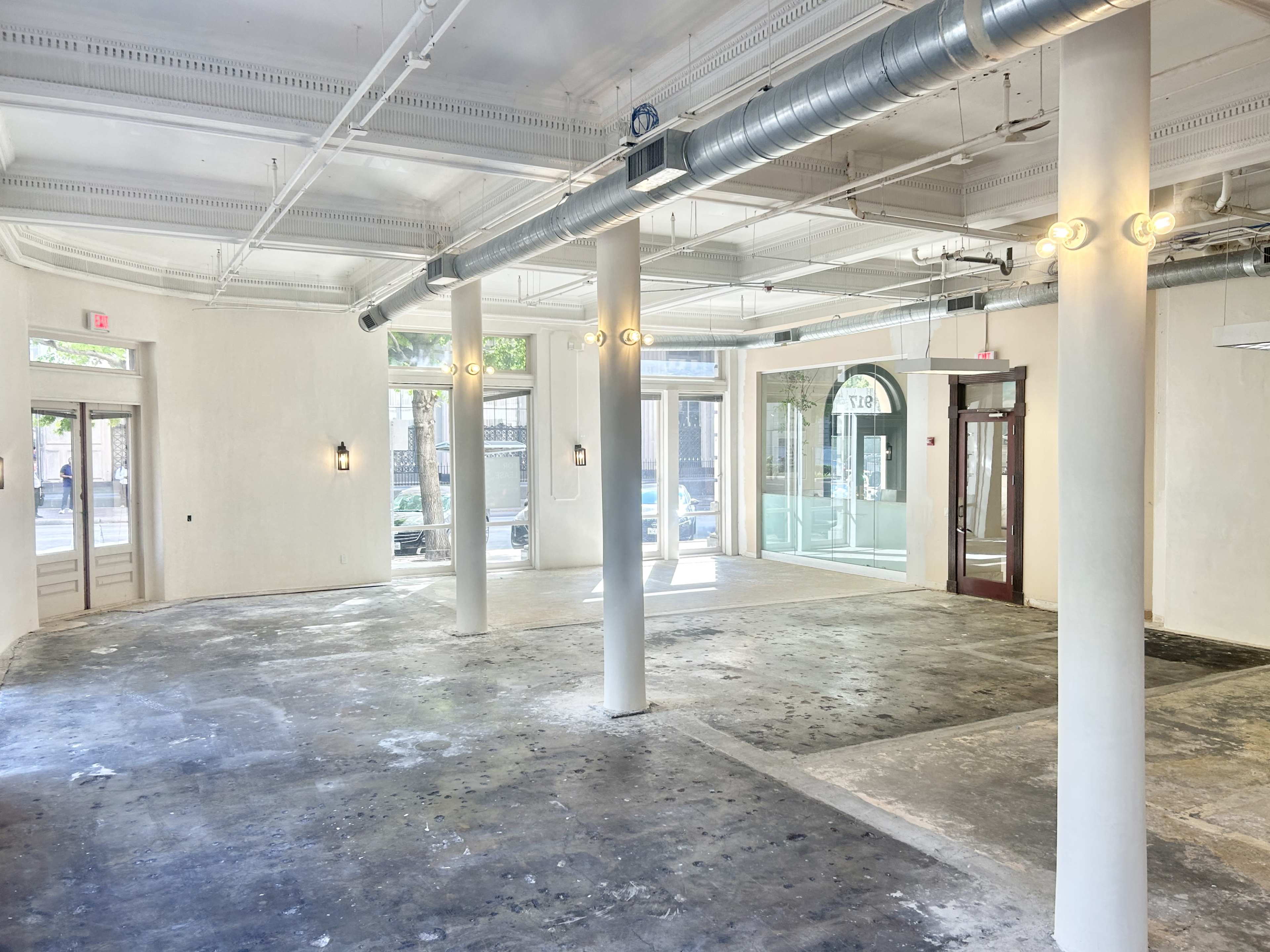 The image shows an empty, spacious interior with exposed columns and large windows, likely a commercial space undergoing renovations.