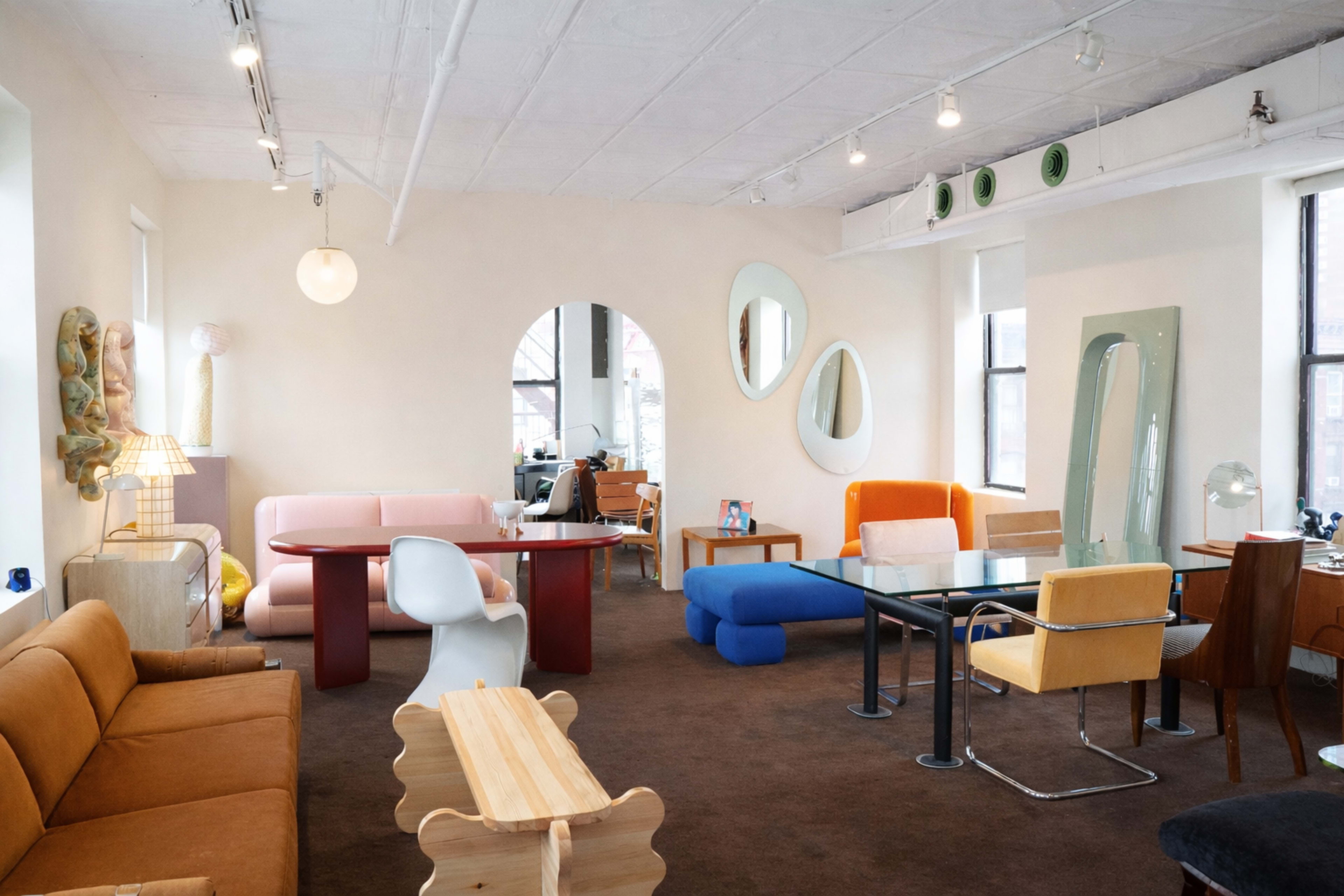 A modern living space features various colorful furniture pieces, including sofas, tables, and chairs, arranged in an open layout.