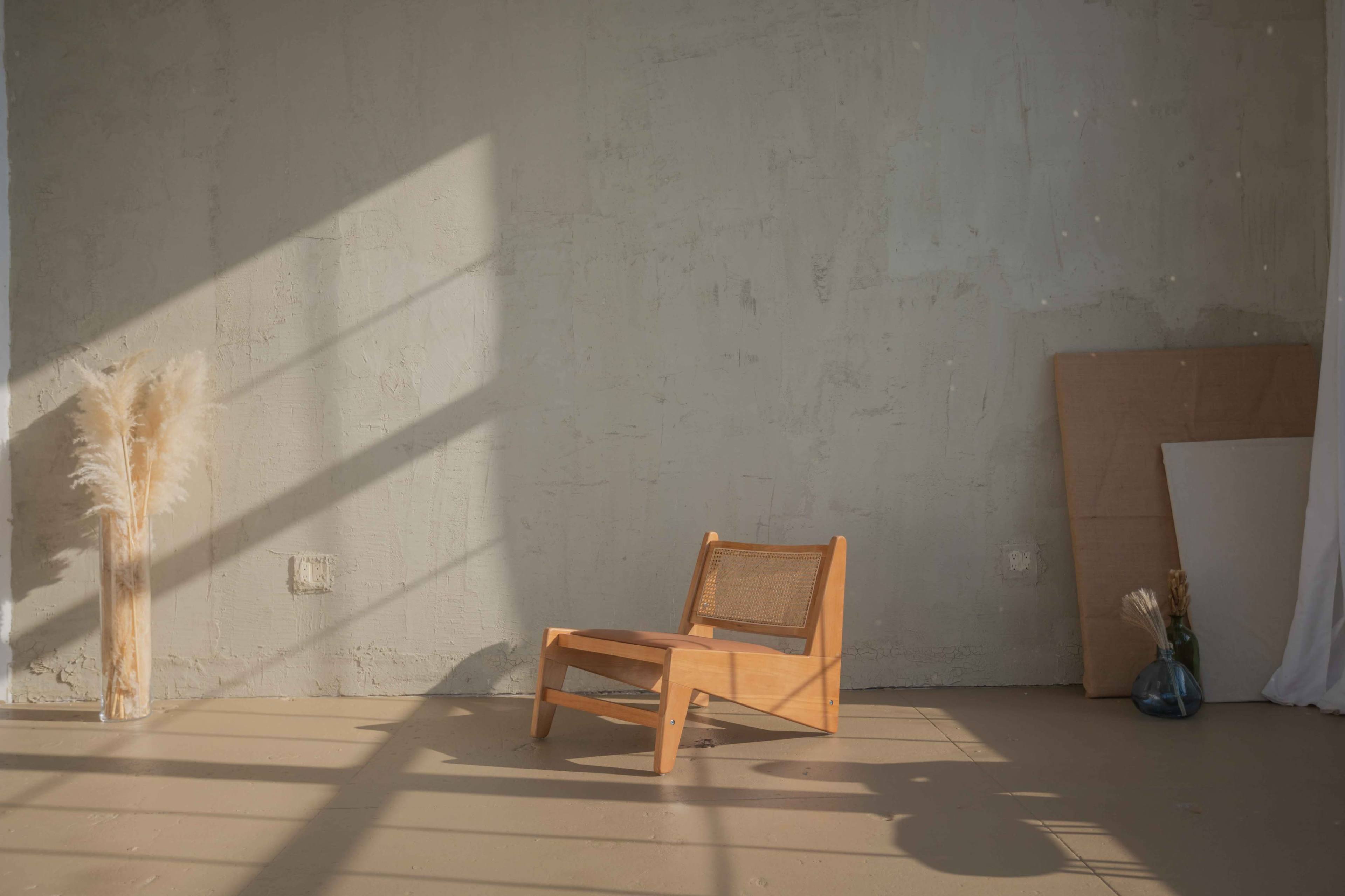 A wooden chair with a woven backrest sits in a sunlit room, casting shadows on a textured wall.