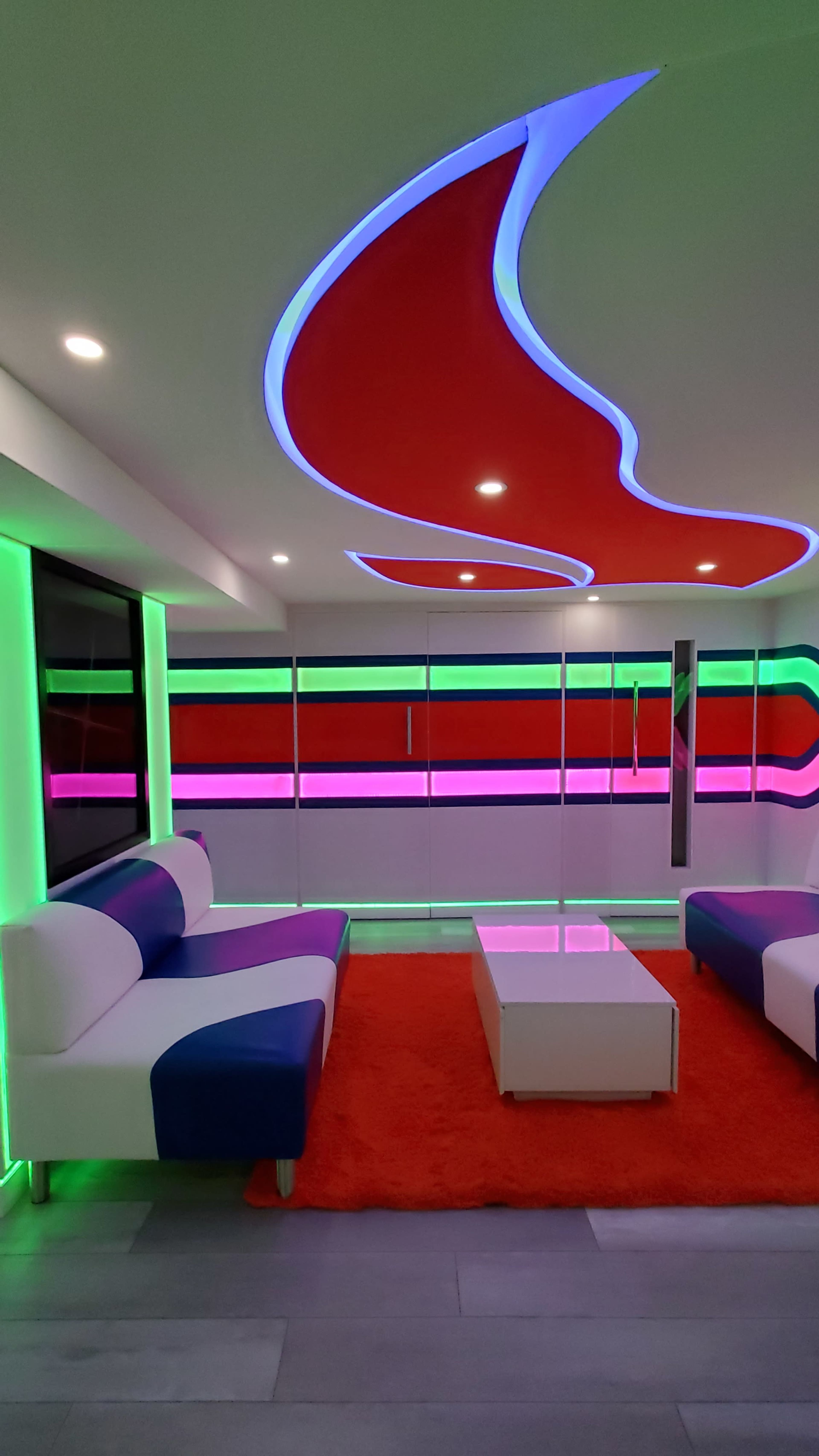 A modern interior with colorful LED lighting, stylish furniture, and a bright rug.