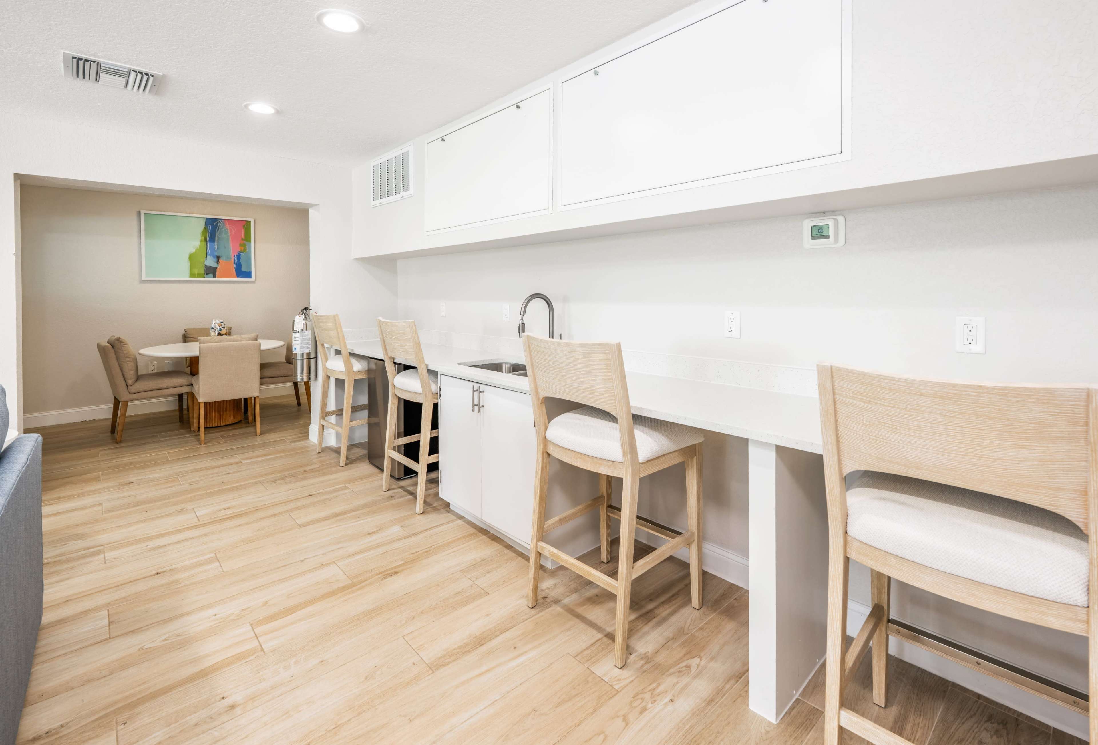 A modern kitchen features white cabinetry, a countertop with bar stools, and light wood flooring.