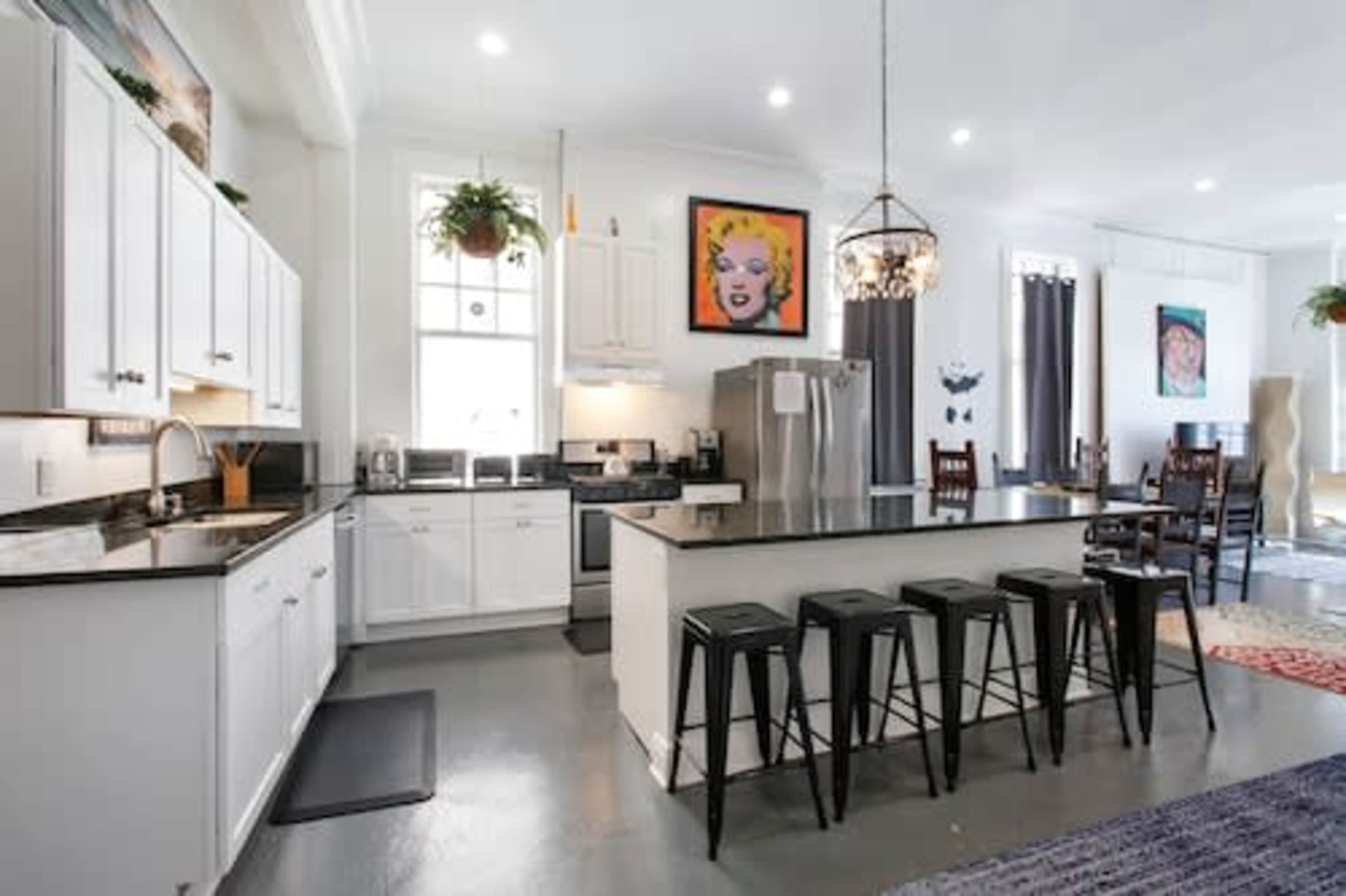A modern kitchen with white cabinetry, a black countertop, stainless steel appliances, and a dining area featuring a wooden table and chairs.