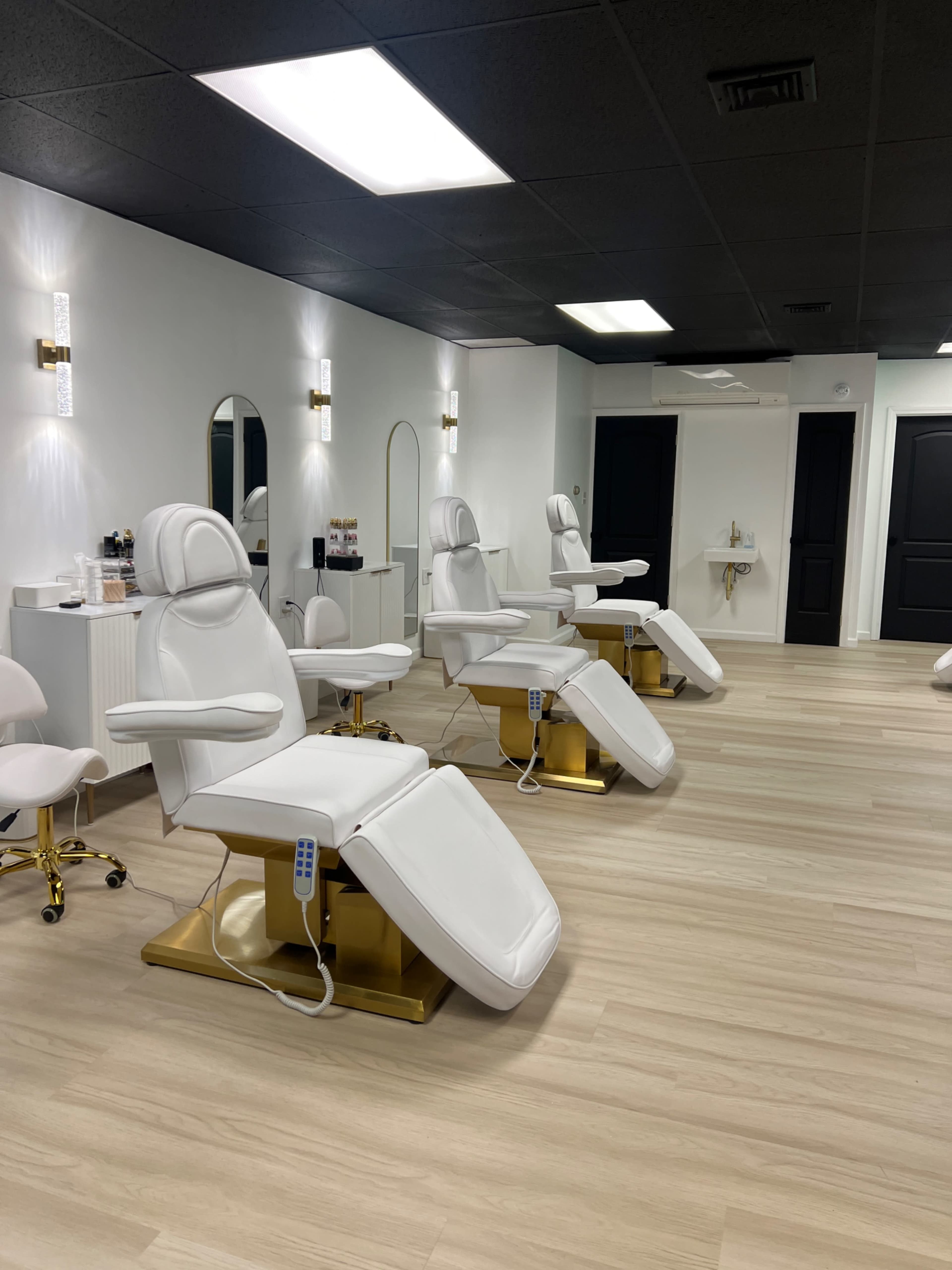 A modern salon interior featuring several white treatment chairs with gold bases arranged in a well-lit space.