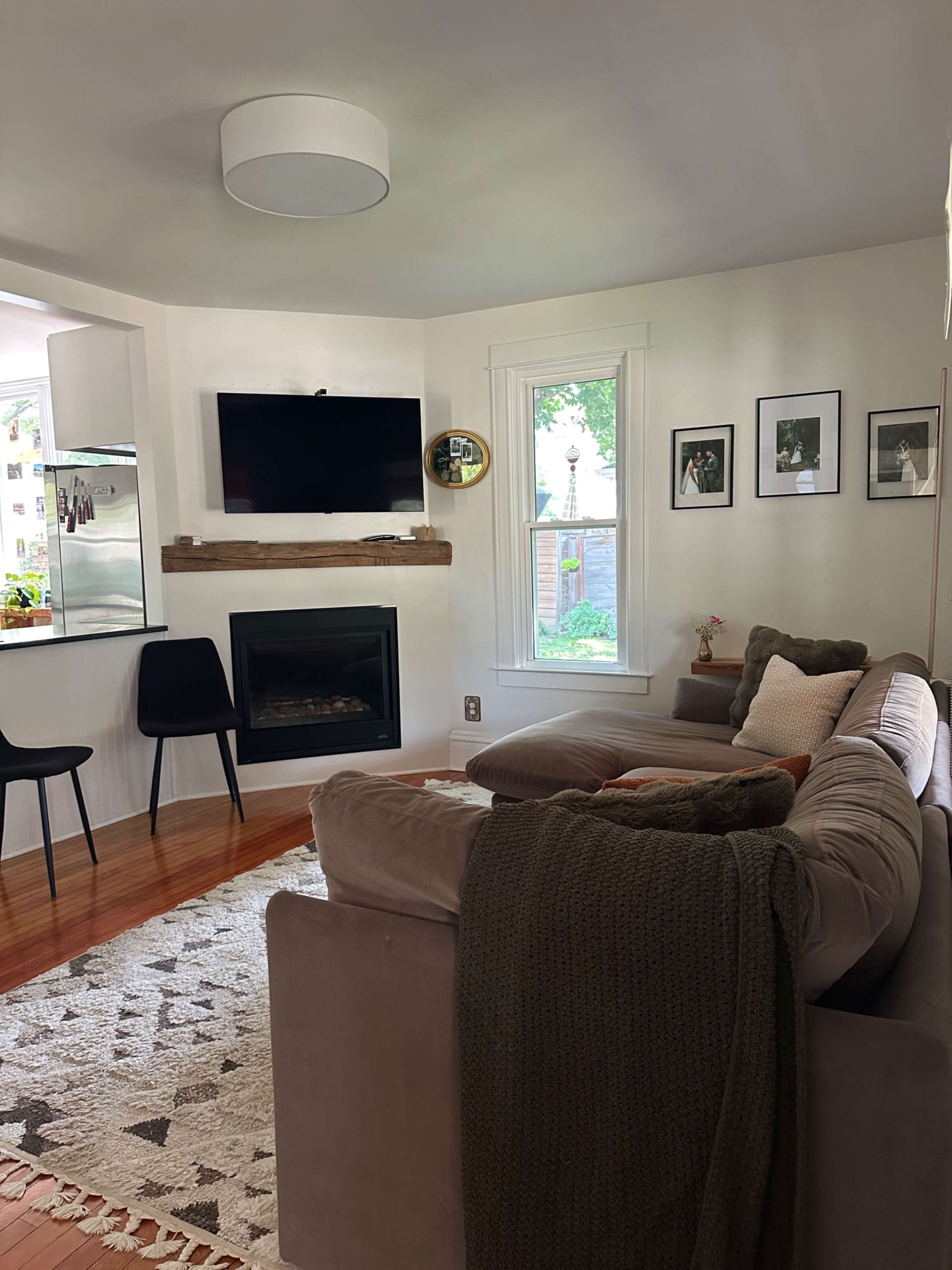 The living room features a gray sectional sofa, a mounted television, a fireplace, and a small dining area with black chairs.