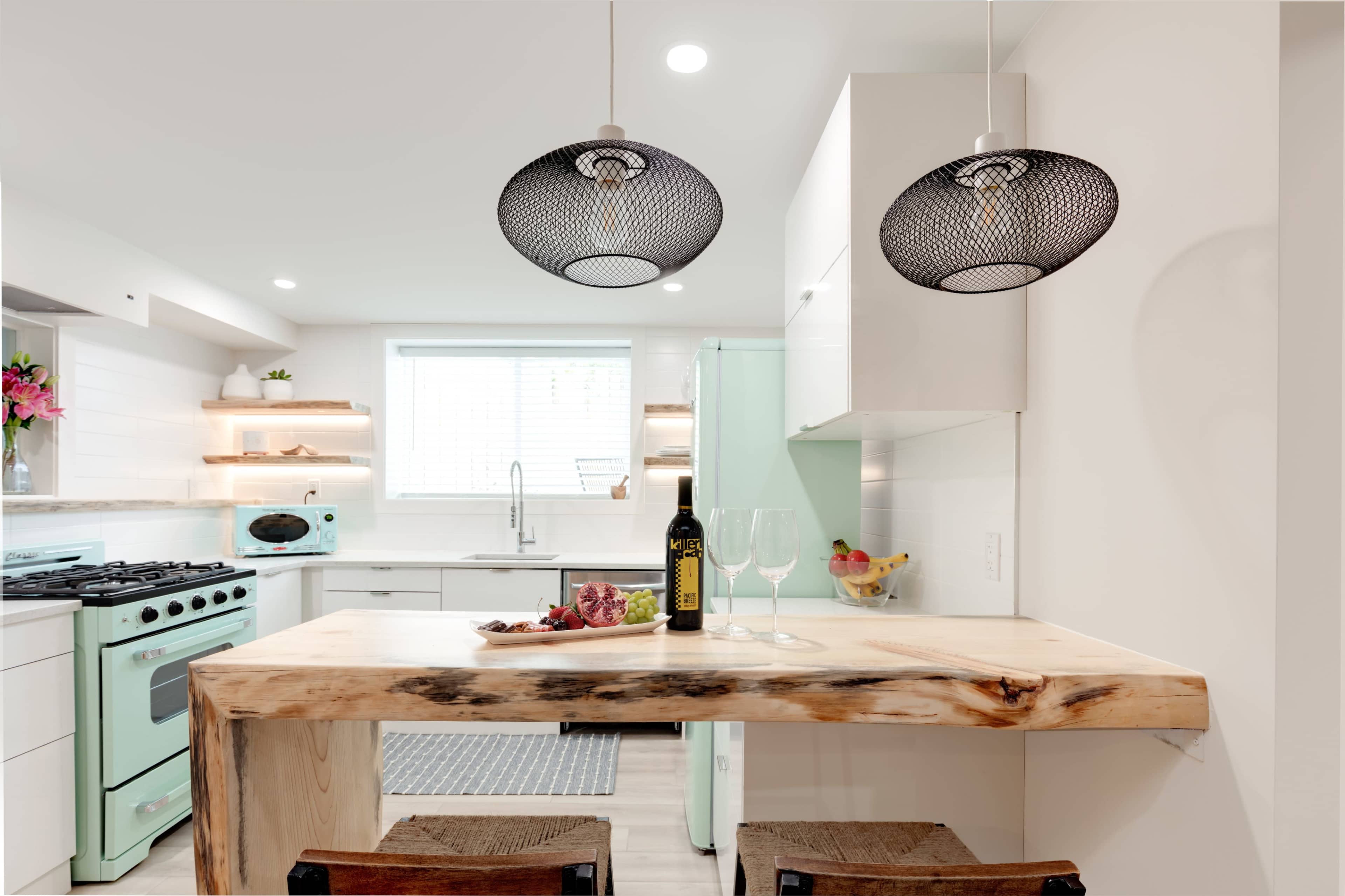 A modern kitchen features a wooden bar table with two chairs, an aqua-colored retro refrigerator, and pendant lights hanging above.