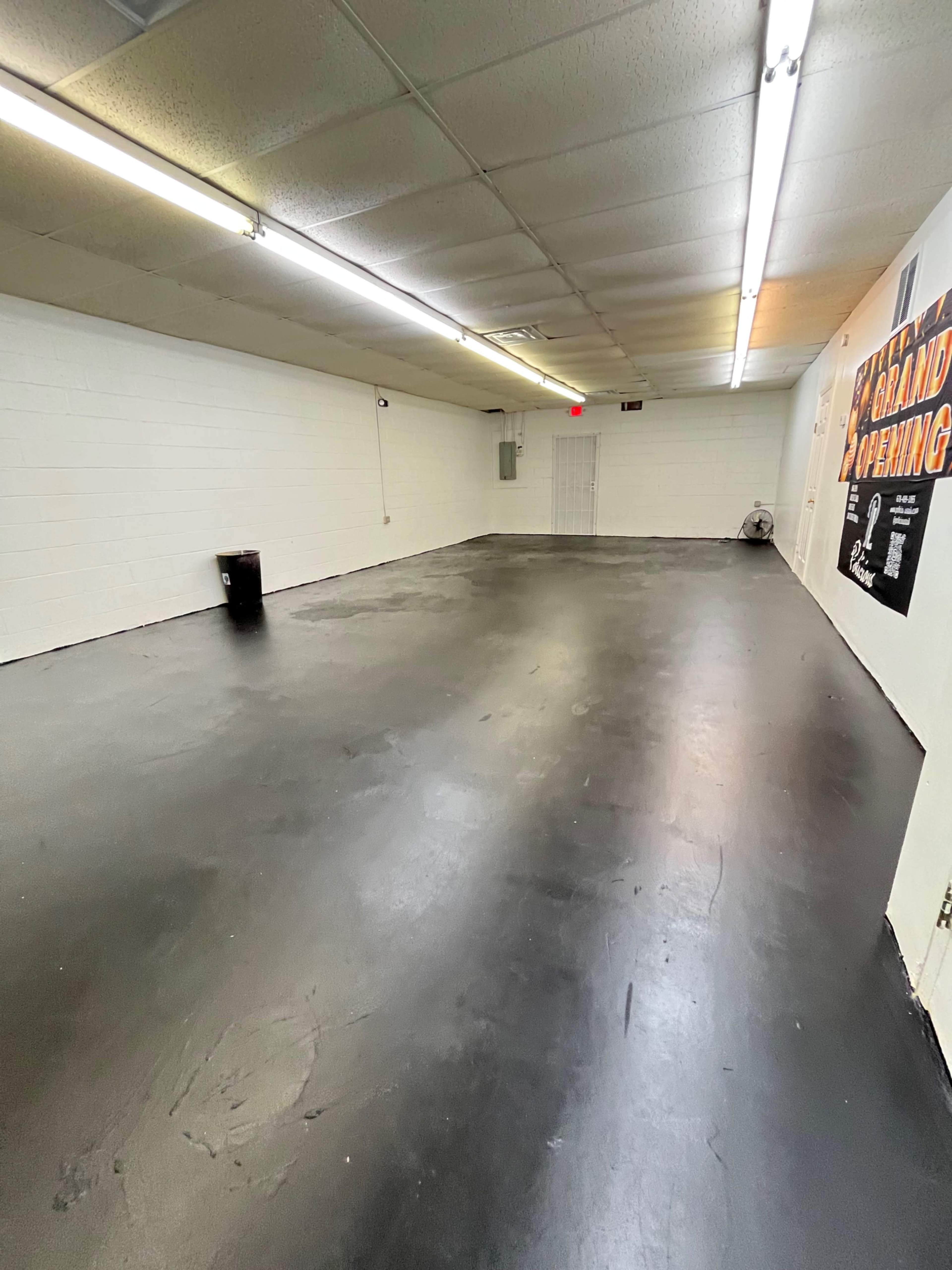 A large, empty room with a black floor, white walls, and overhead fluorescent lighting.