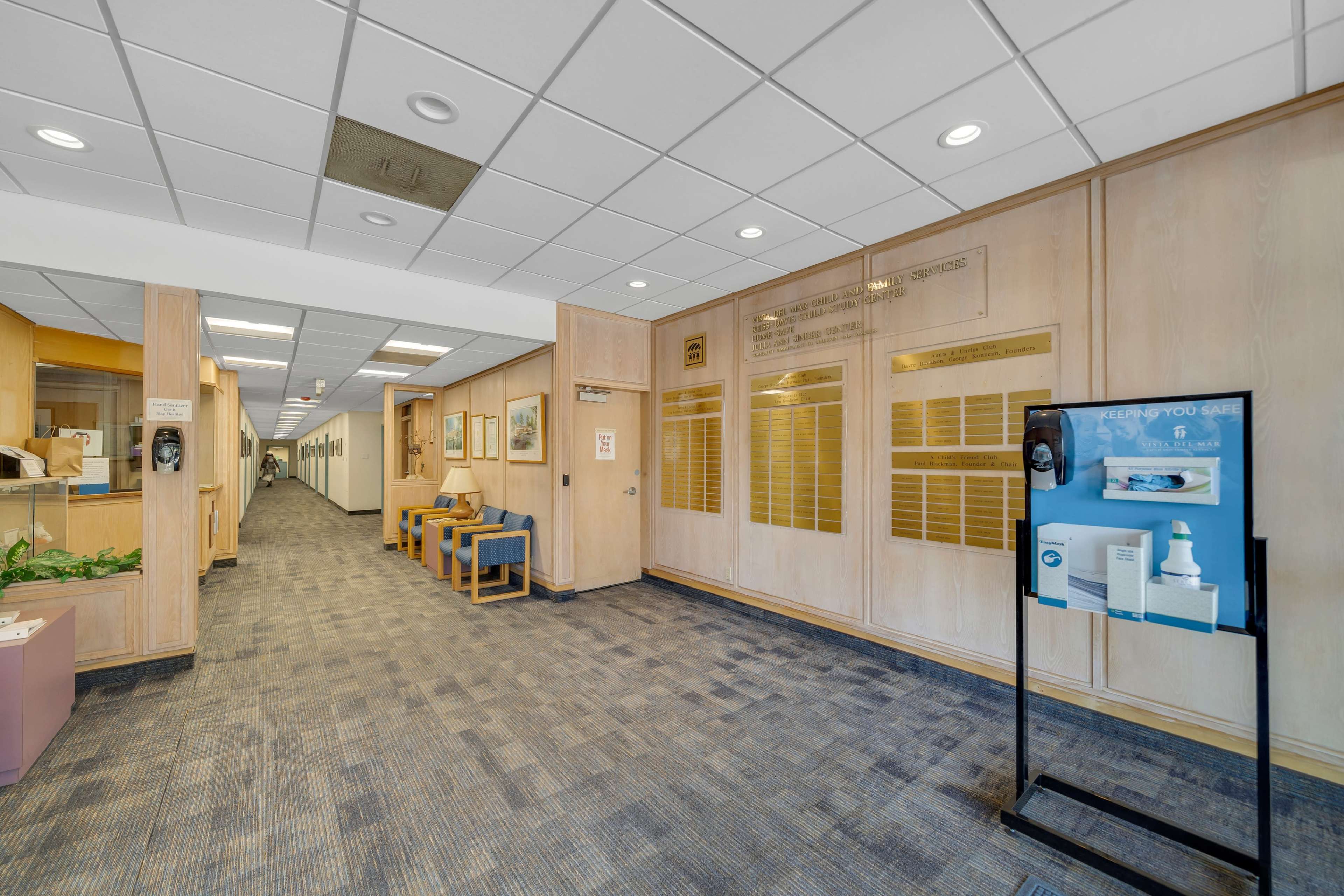 A well-lit hallway with a carpeted floor, wooden paneling, and display boards on the walls.