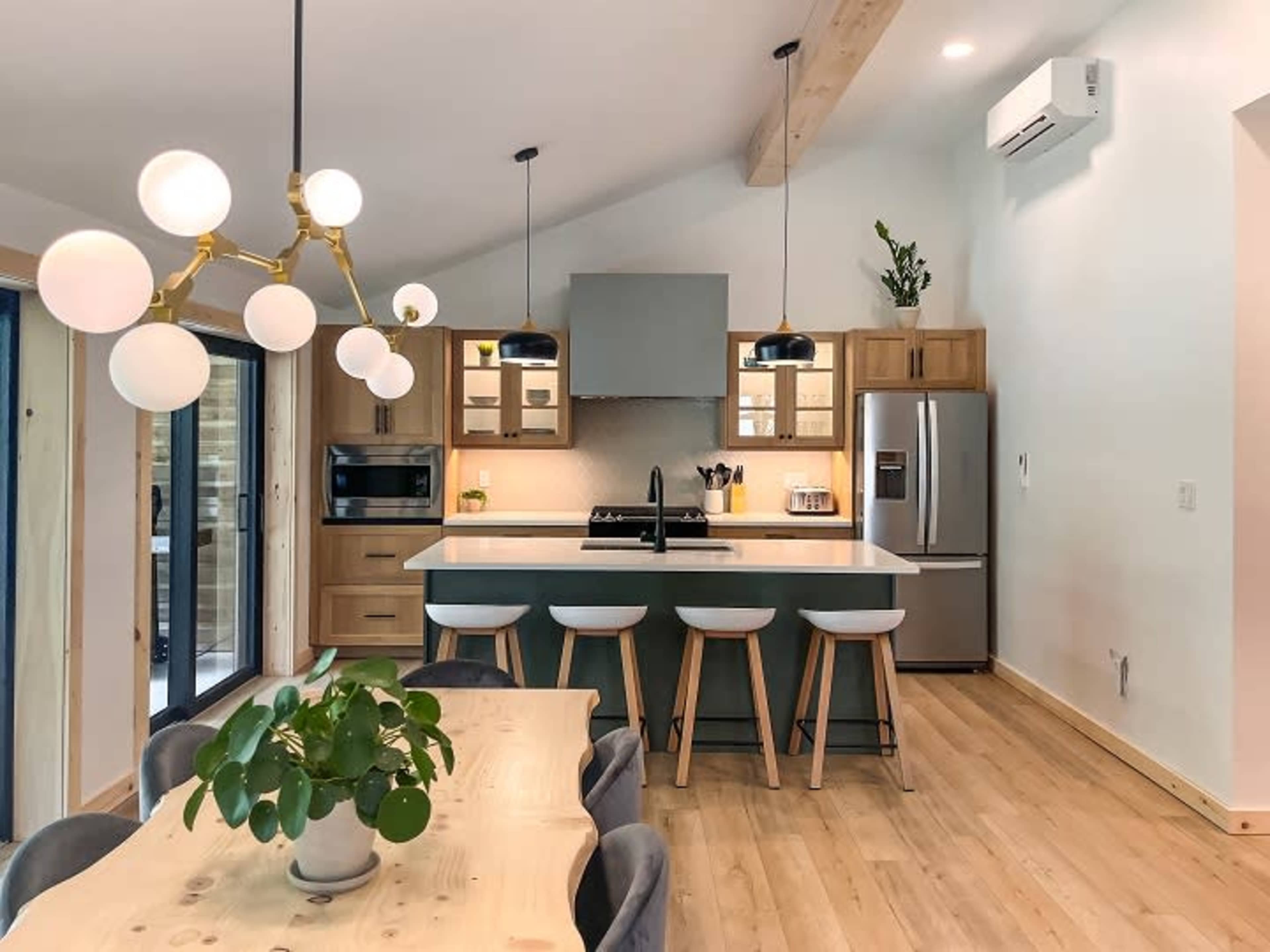 A modern kitchen with a central island, wooden cabinets, a dining table, and pendant lighting.