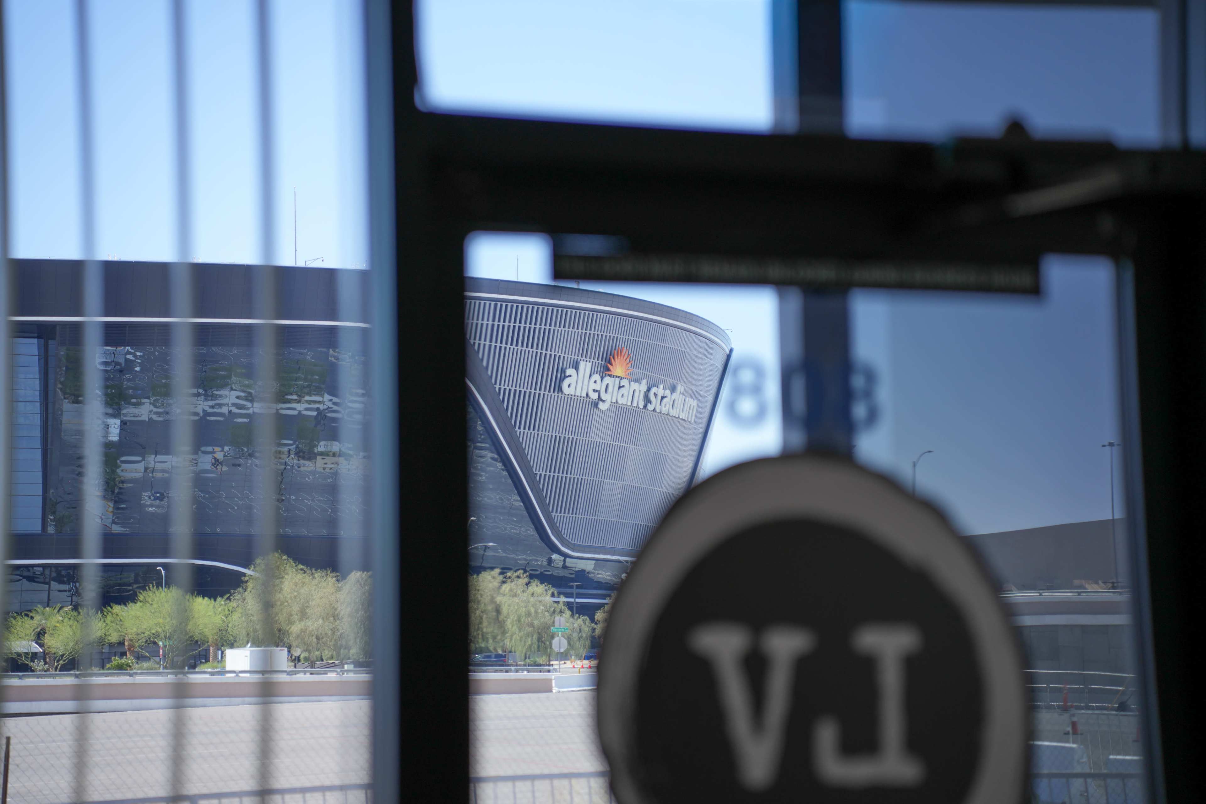 The image shows Allegiant Stadium visible through a glass door, framed by the door's circular handle.
