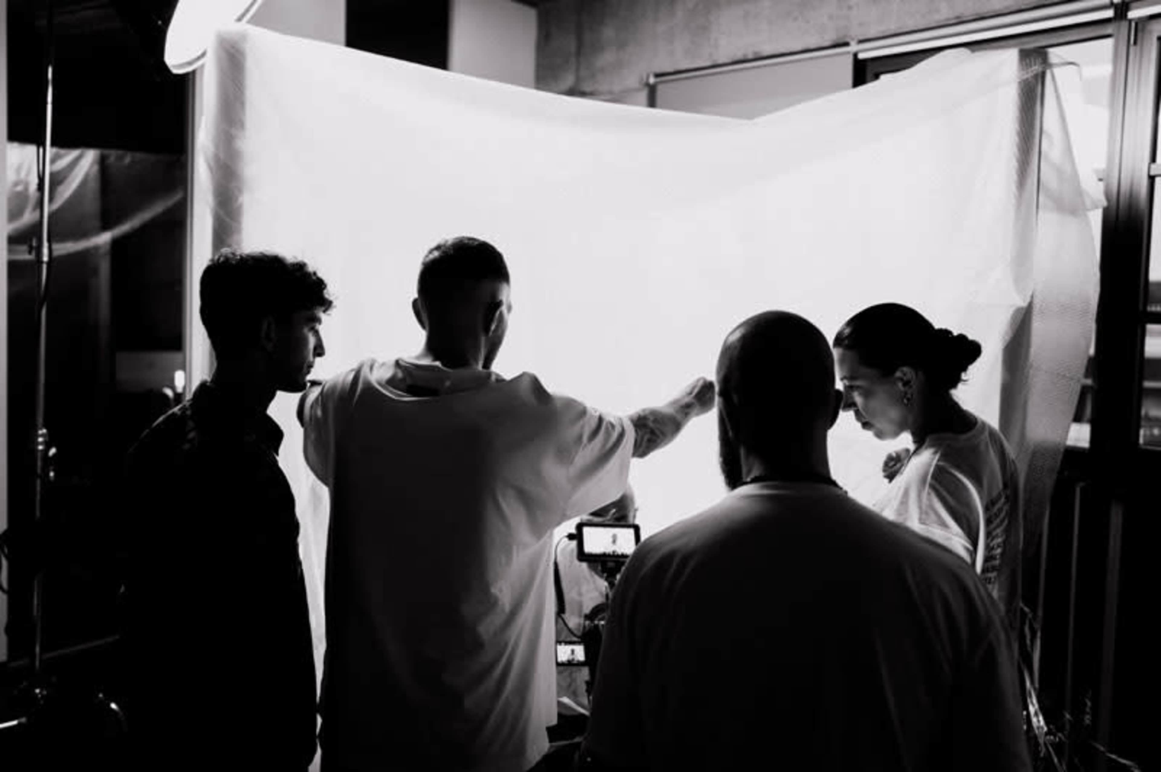 A group of four people is positioned around a translucent screen while one person adjusts their arms to control the lighting in a creative studio setting.