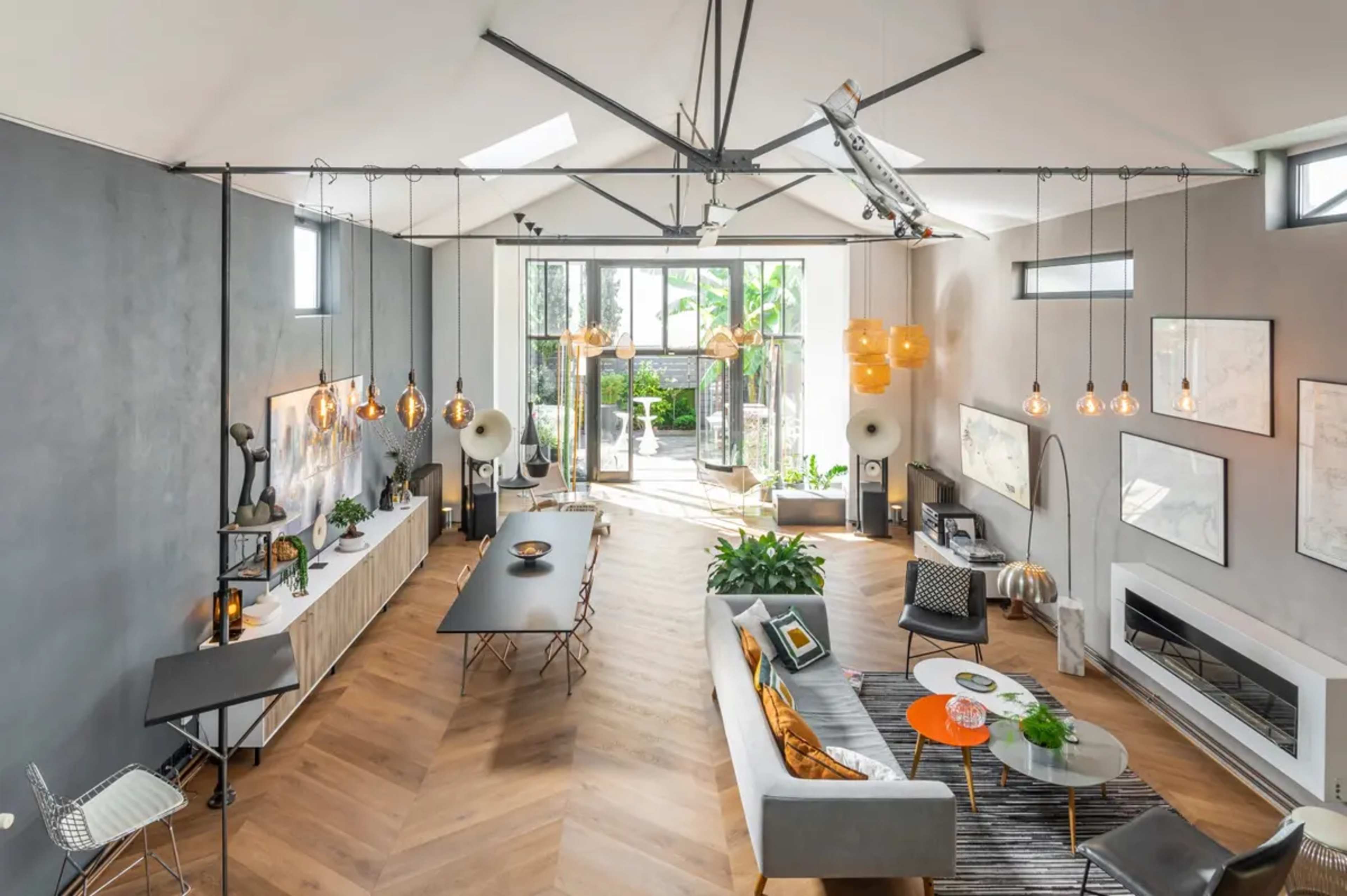 A modern open-plan living space with a dining area, a lounge, and large windows that lead to an outdoor patio, featuring wooden flooring and contemporary furnishings.