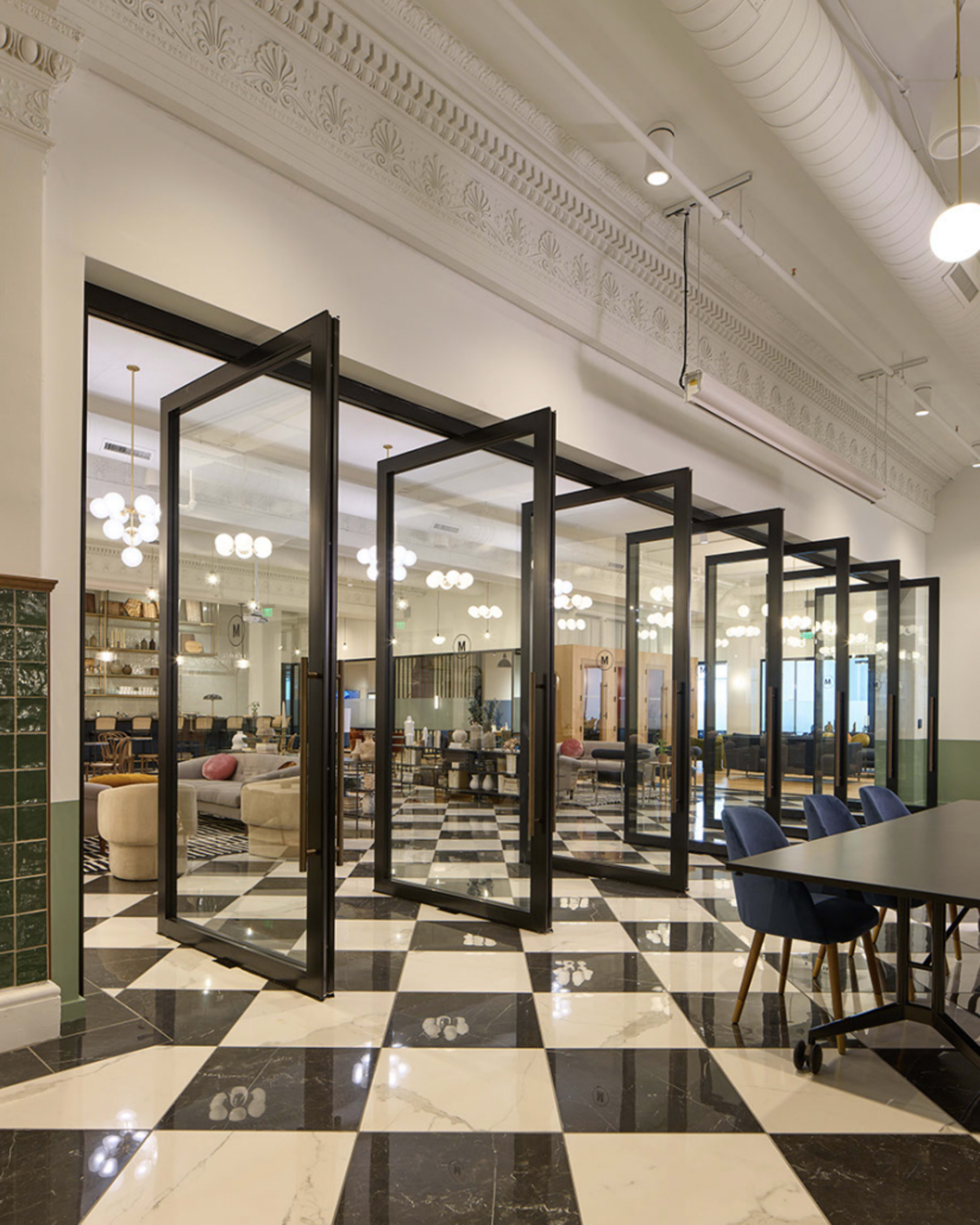 A modern office space with large glass doors separating multiple meeting rooms, featuring a checkered black and white floor.