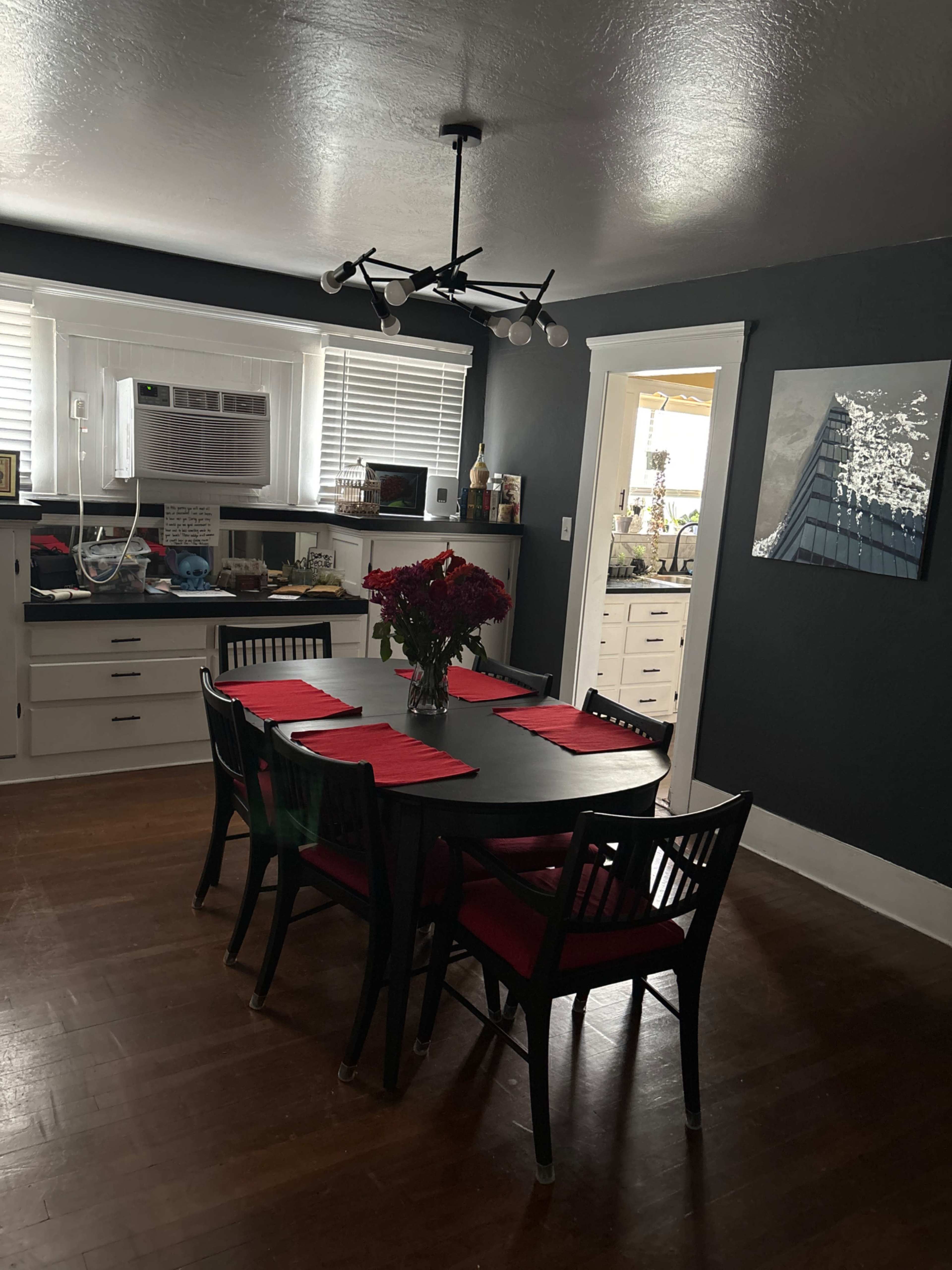 A dining room with a black table set with red placemats, surrounded by black chairs, and an air conditioning unit in a white window.