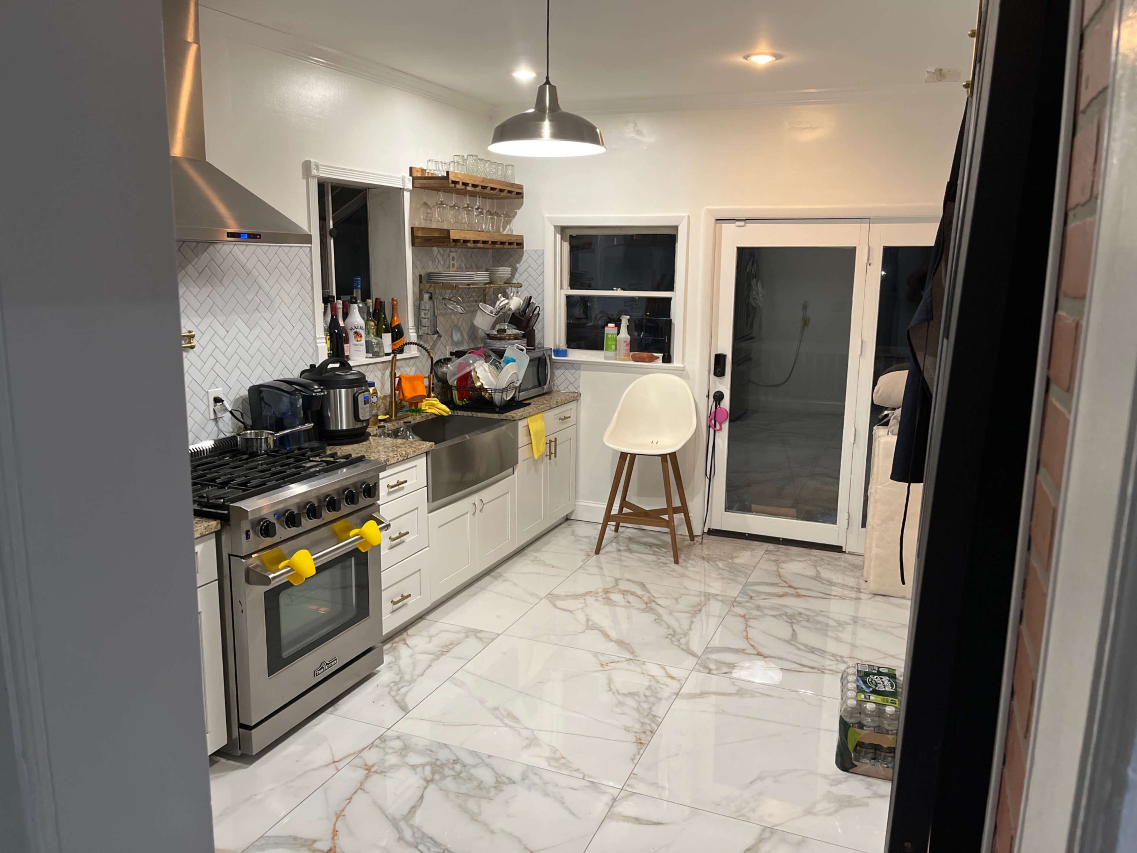 A modern kitchen with a marble floor, stainless steel appliances, and a combination of open shelves and cabinetry.