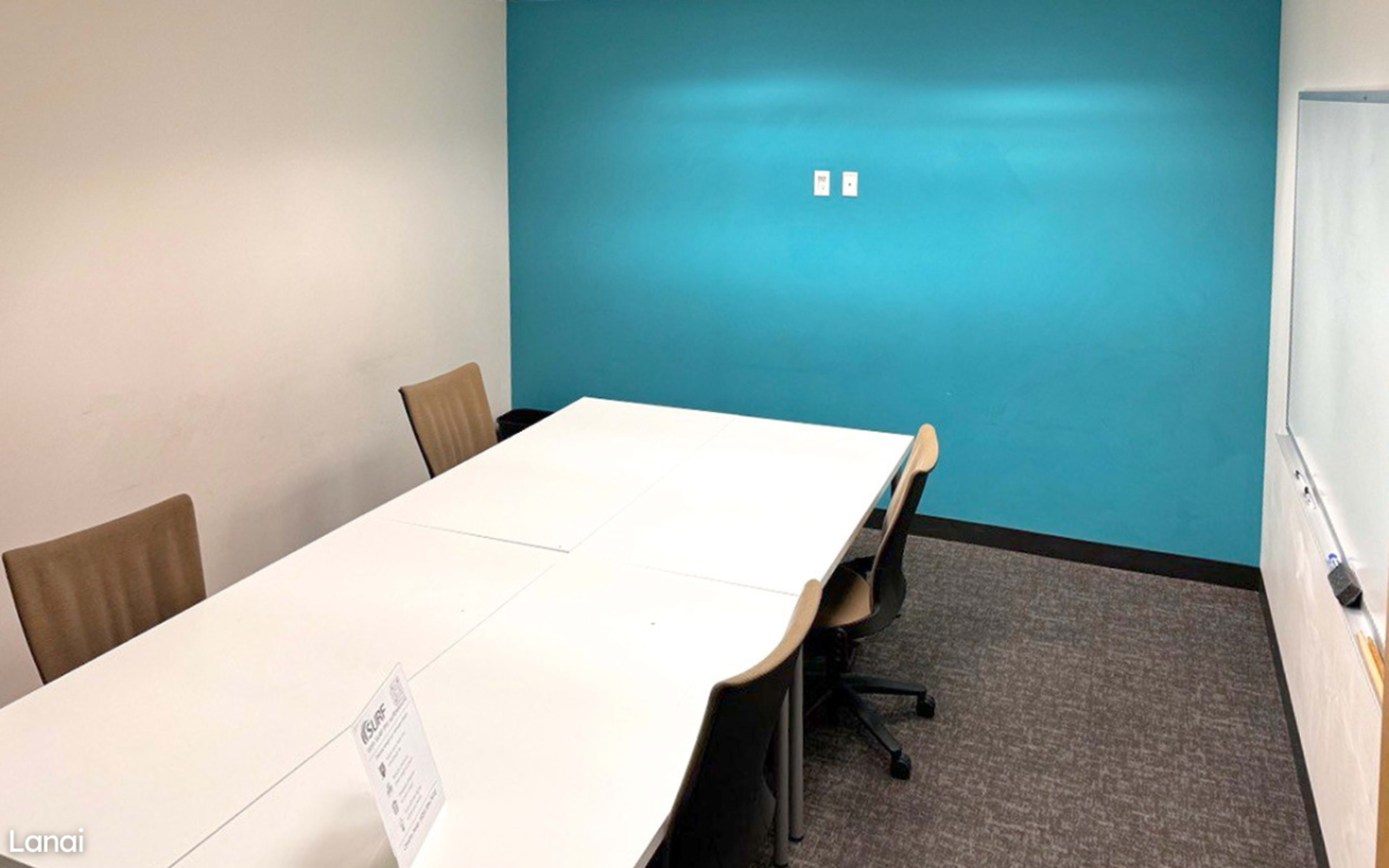 A small conference room with a white table, four chairs, a blue wall, and a whiteboard.