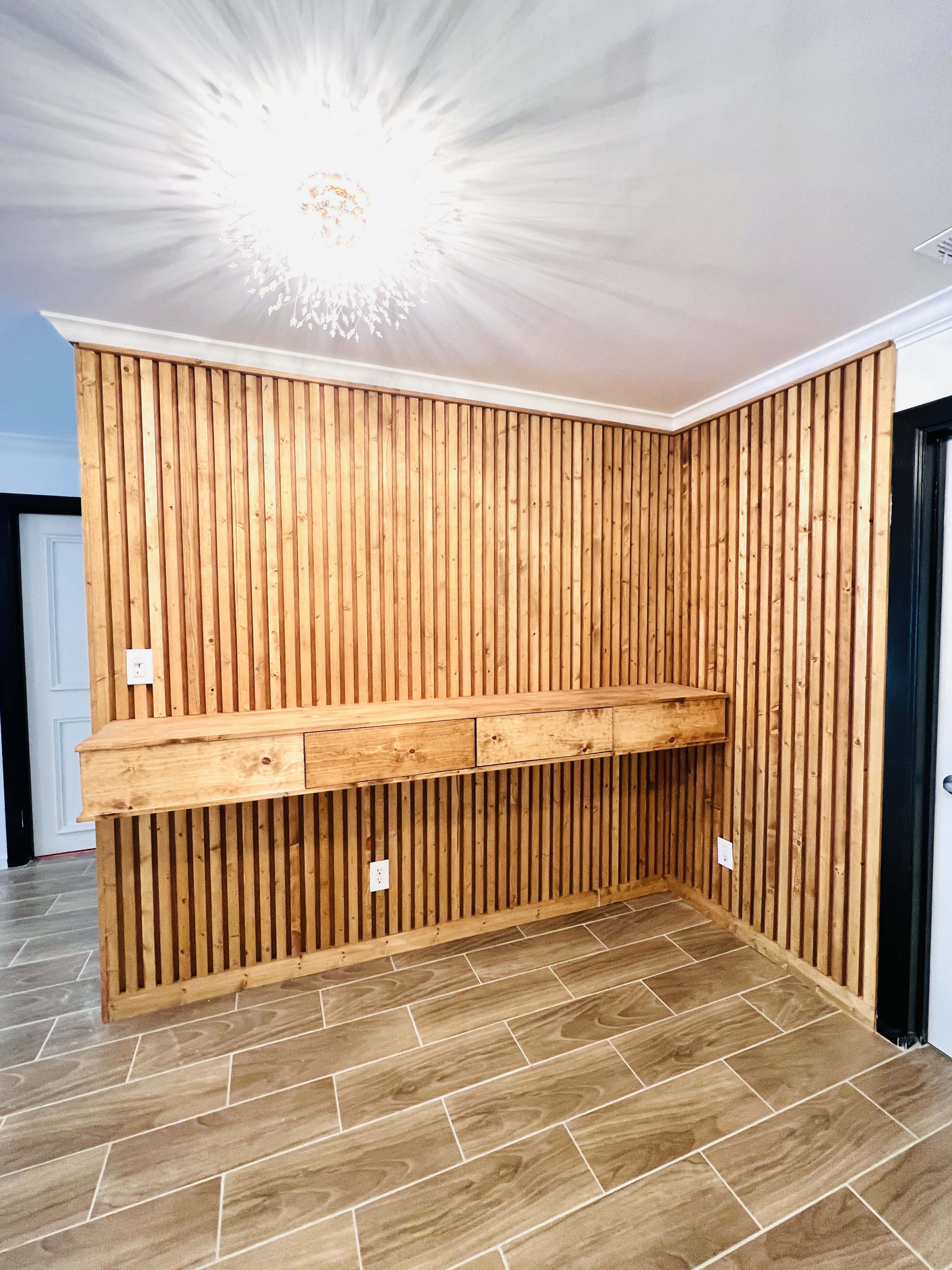 A room with wooden slat walls and a built-in wooden shelf under a decorative light fixture.