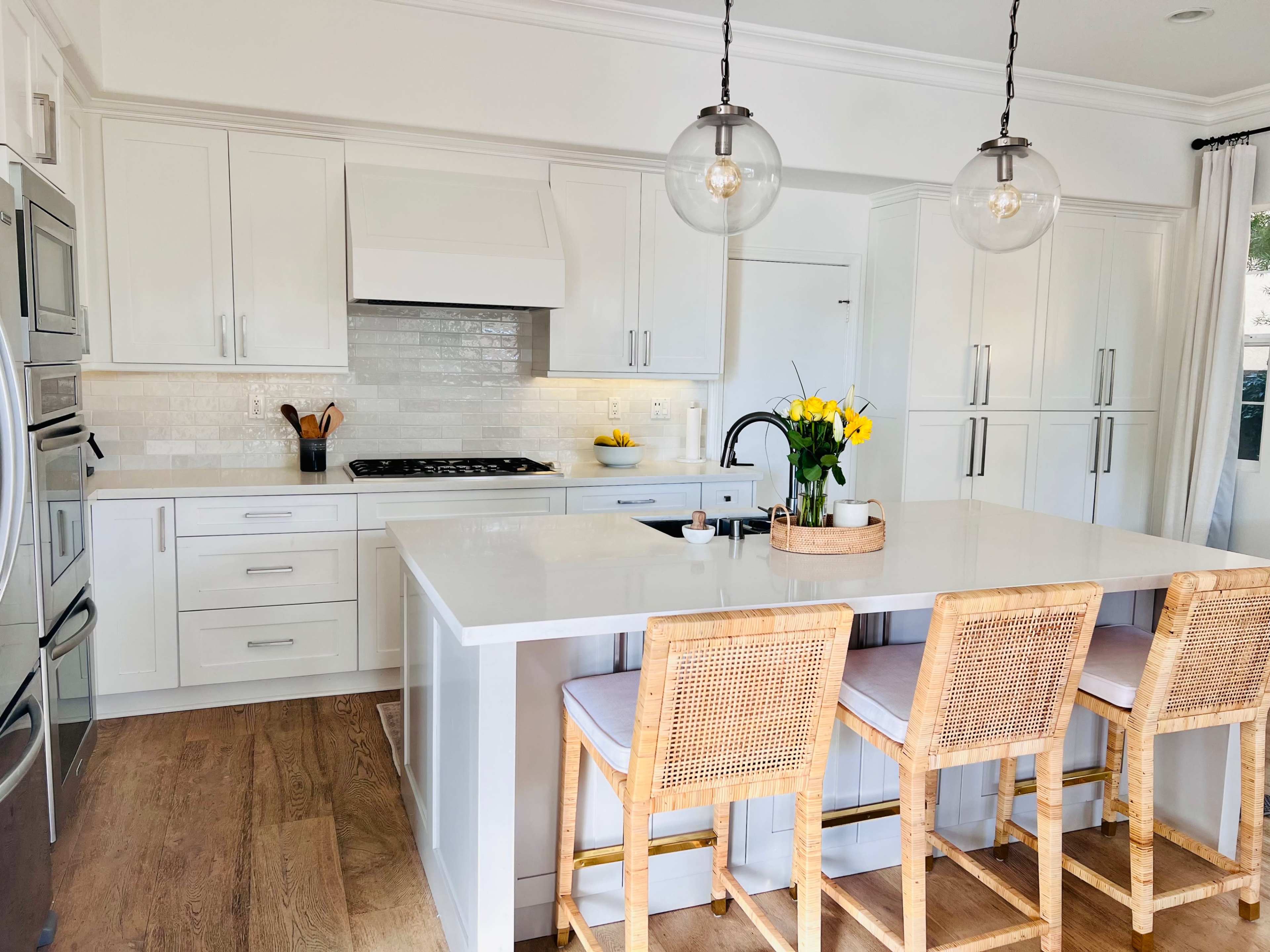A modern kitchen features white cabinetry, a large island with bar stools, and pendant lighting, with fresh flowers on the counter.