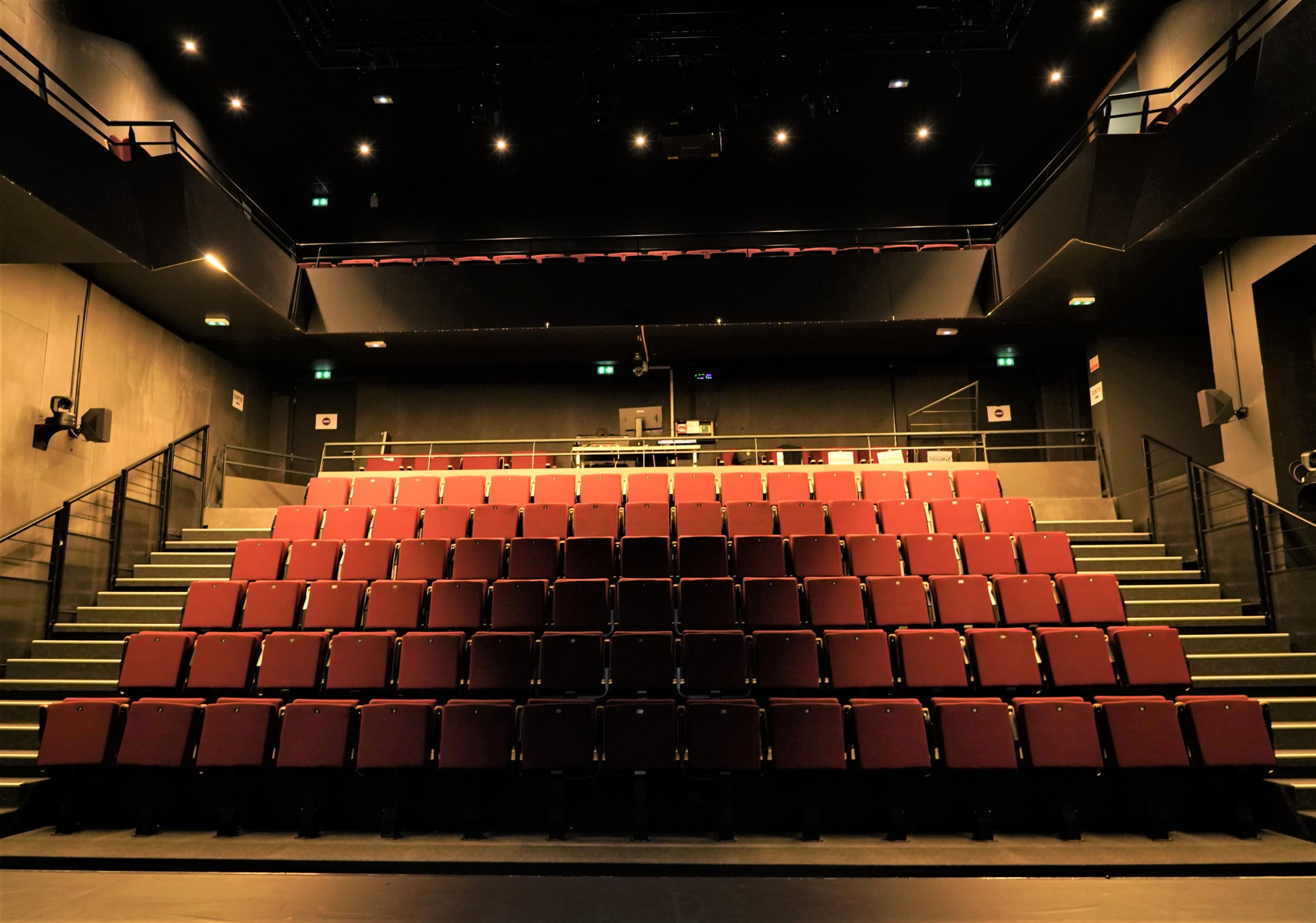 A dimly lit theater with rows of maroon seats arranged in a steeply tiered configuration.