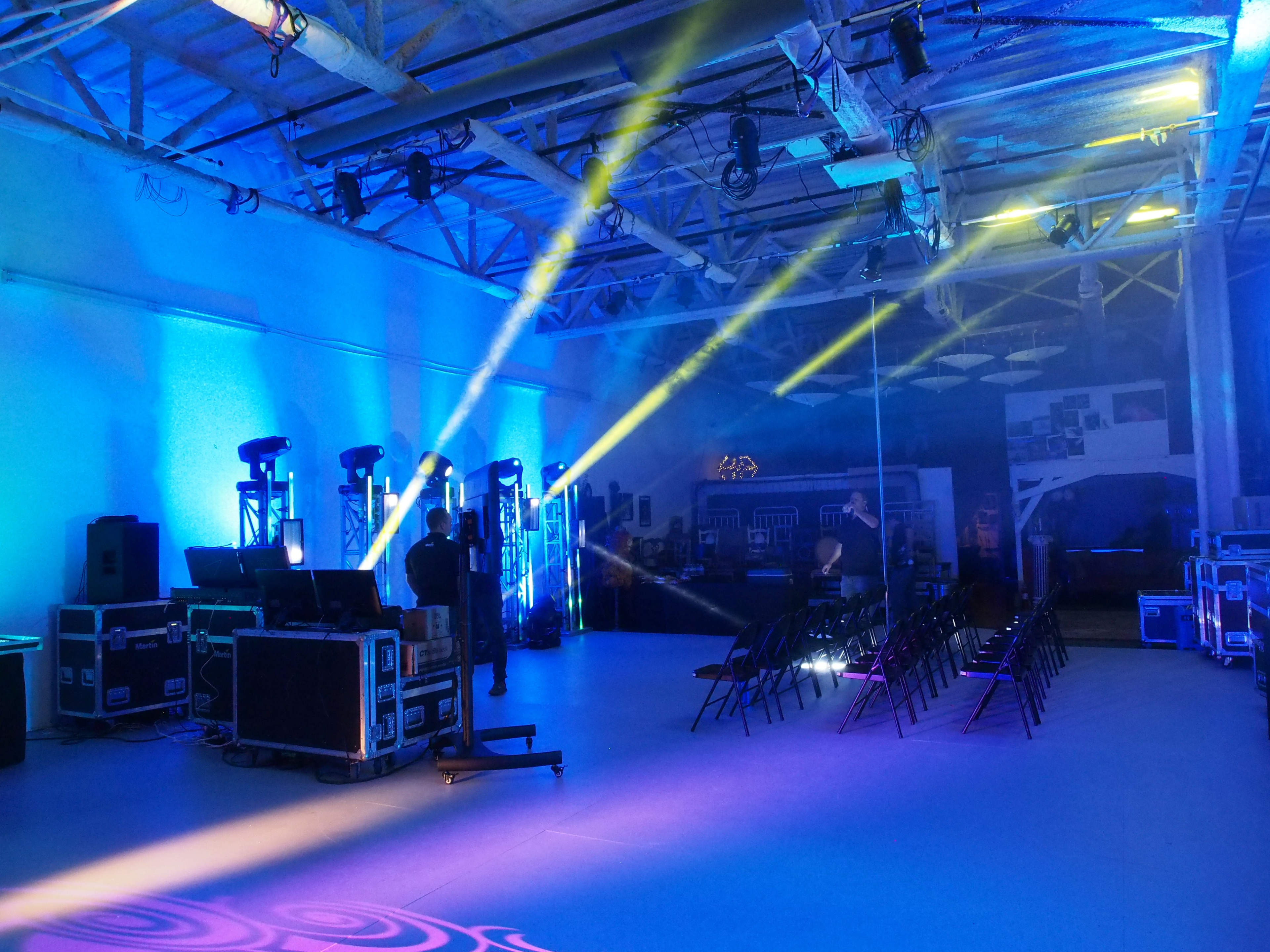 An empty event space with rows of chairs, lighting rigs, and equipment set up for a performance or gathering.