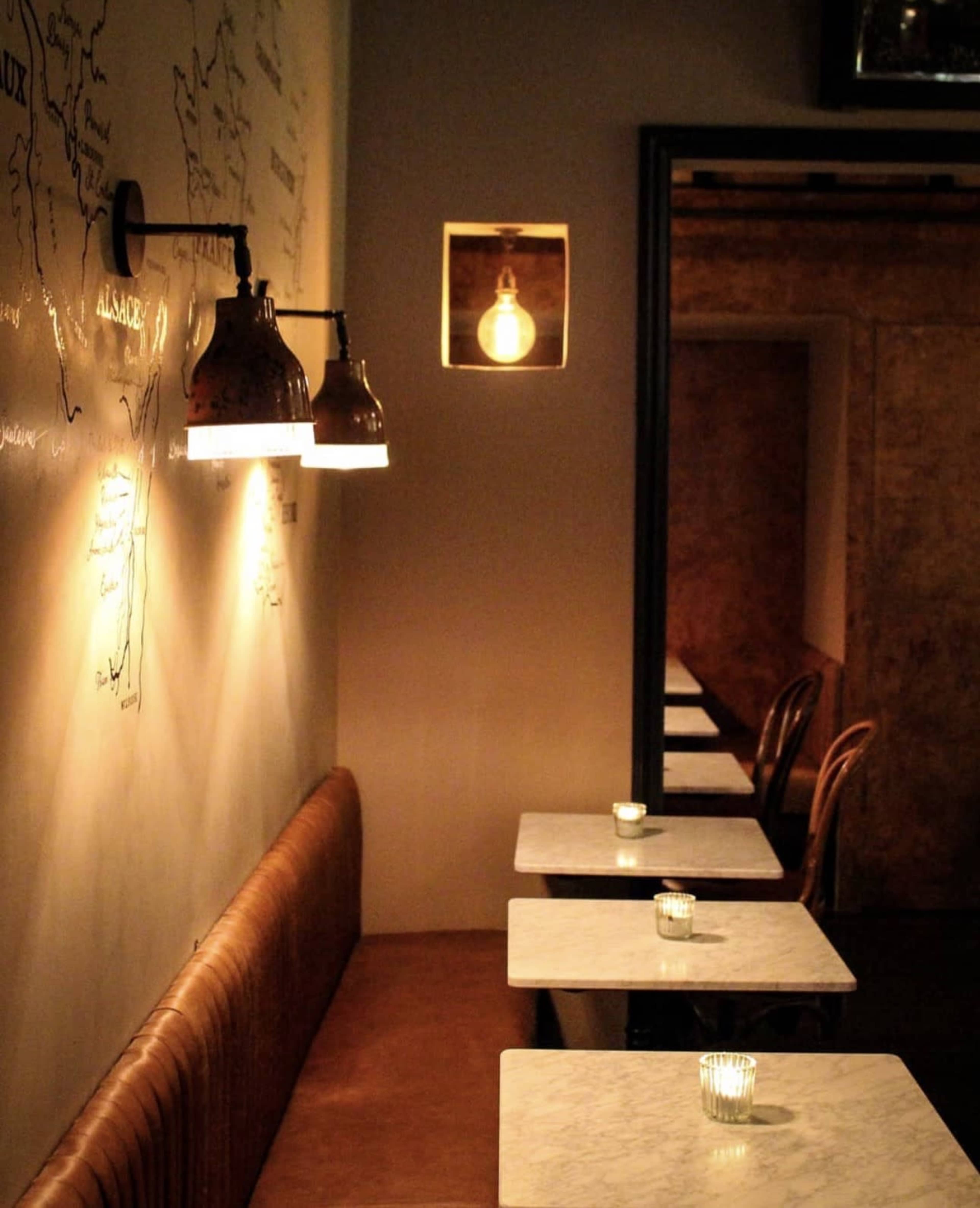 A dimly lit restaurant interior features marble-top tables, a wall decorated with maps, and exposed light fixtures.