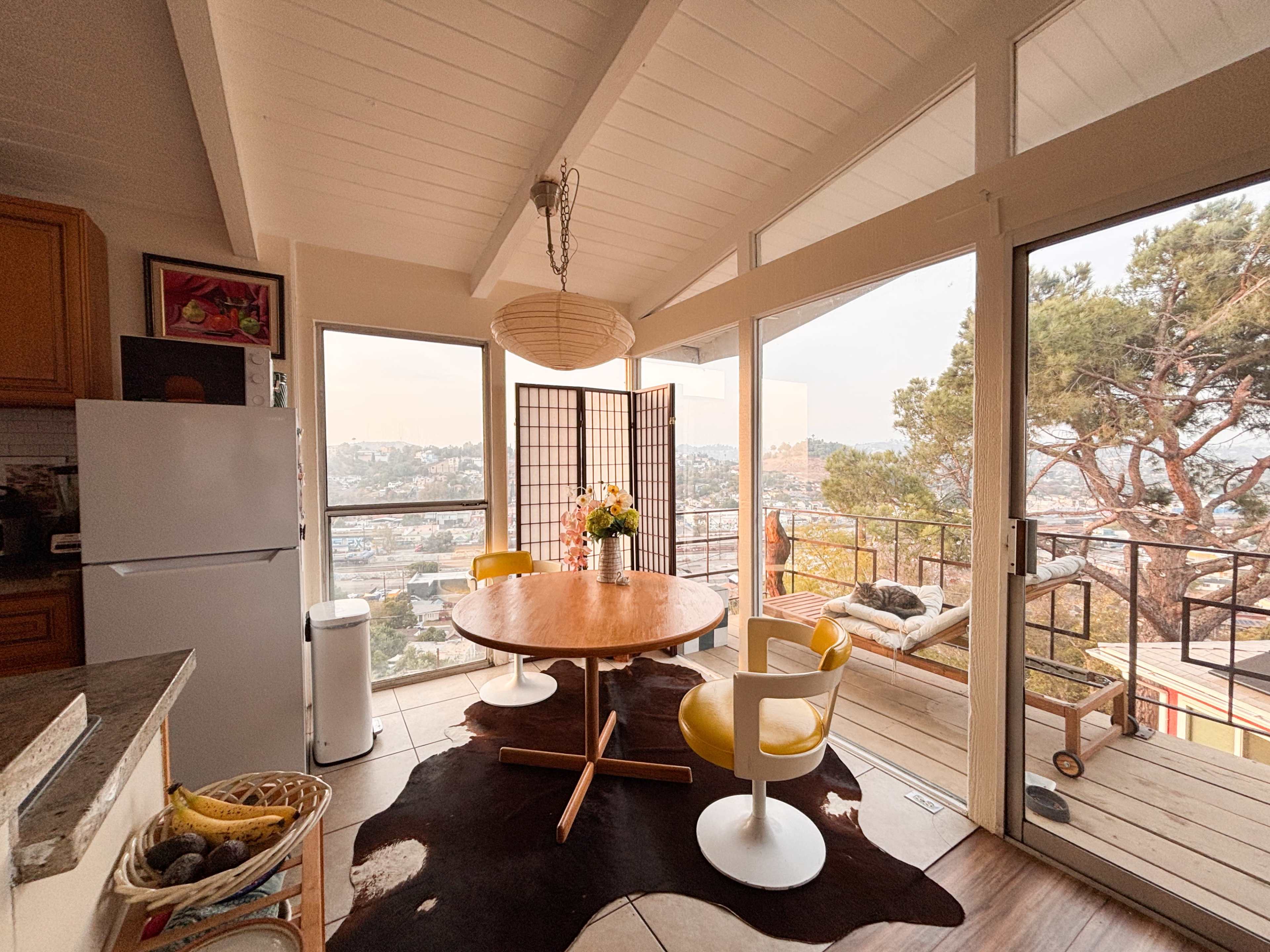 A modern kitchen features a round wooden table with two chairs and a view of the outdoors through large windows.