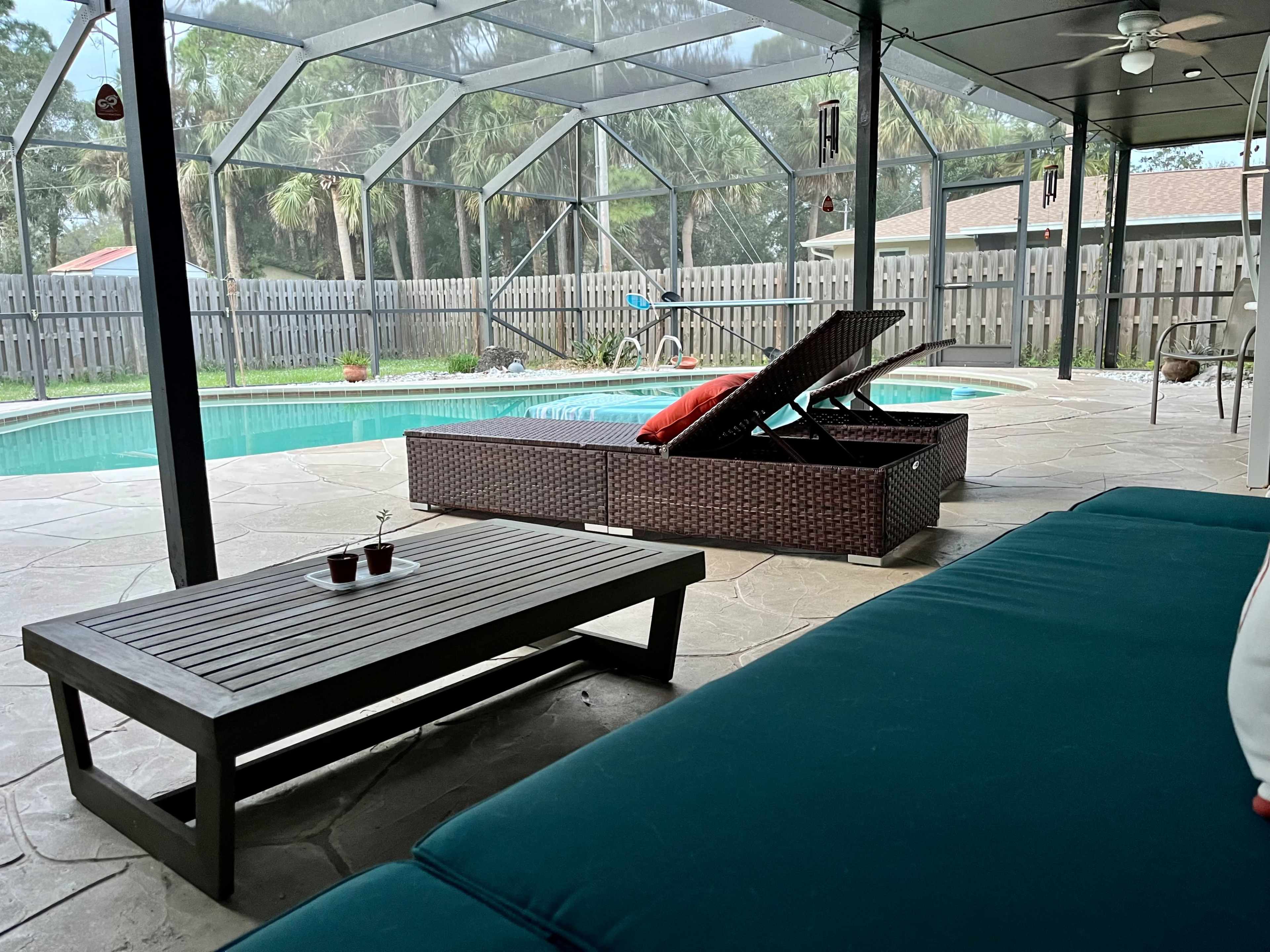 A screened-in patio area with a swimming pool, a lounge chair, and a table with small potted plants.