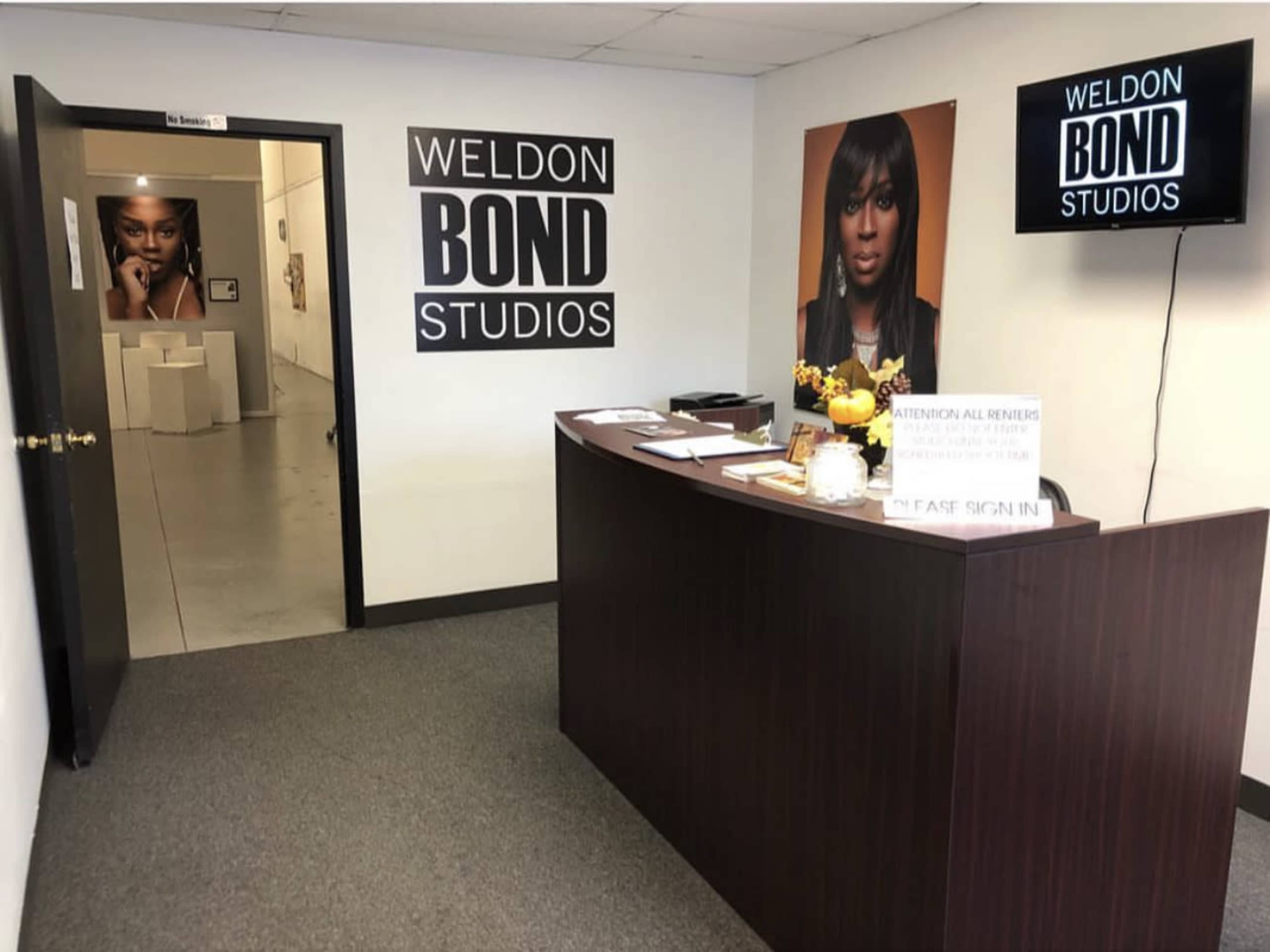 A reception area of Weldon Bond Studios featuring a desk with paperwork, a fruit bowl, and wall art depicting a woman's portrait.