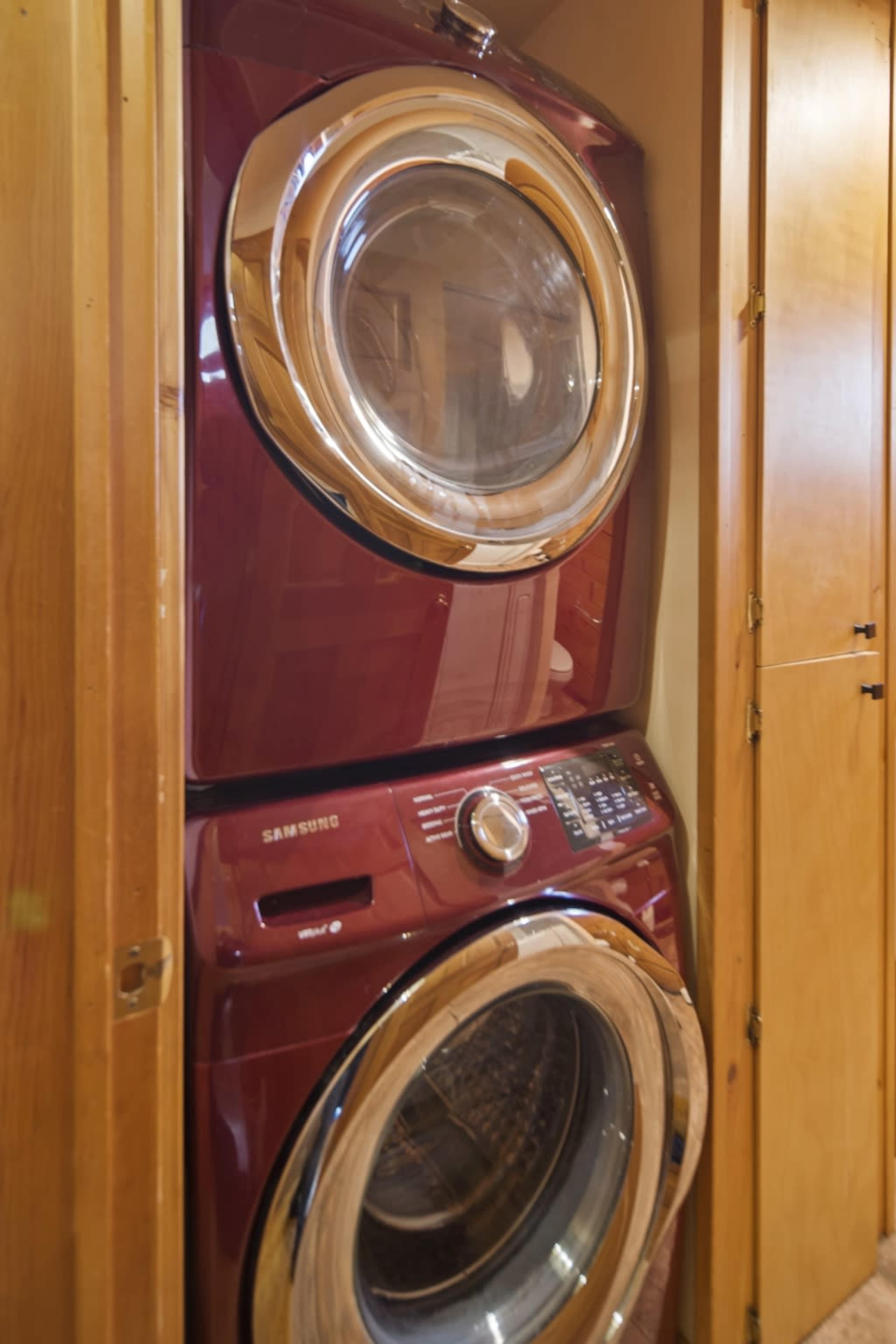 A stacked red Samsung washer and dryer are installed in a wooden cabinet.