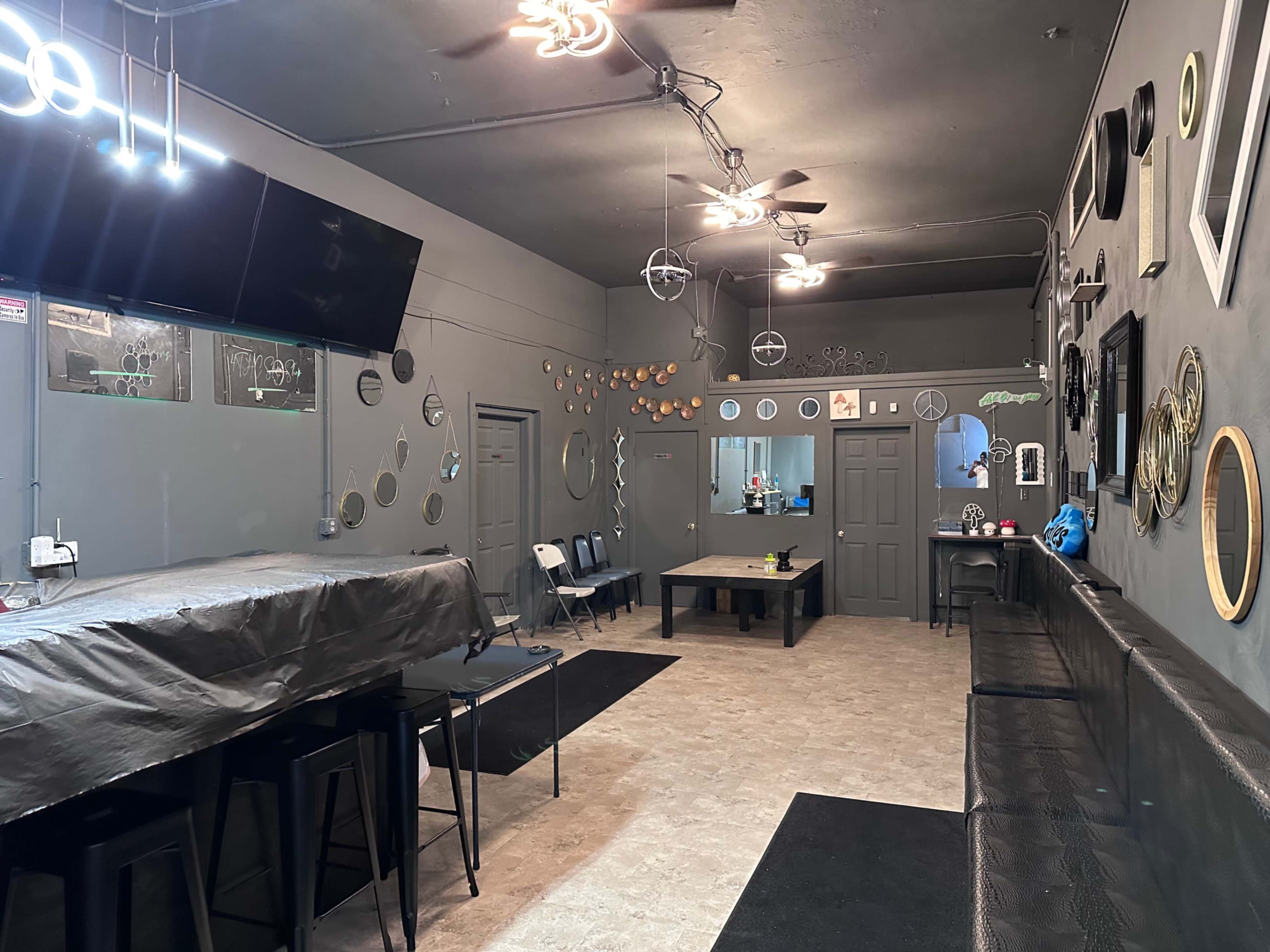 The image shows a spacious, dimly lit room with a long bar, several tables, and various decorative circular mirrors on the walls.