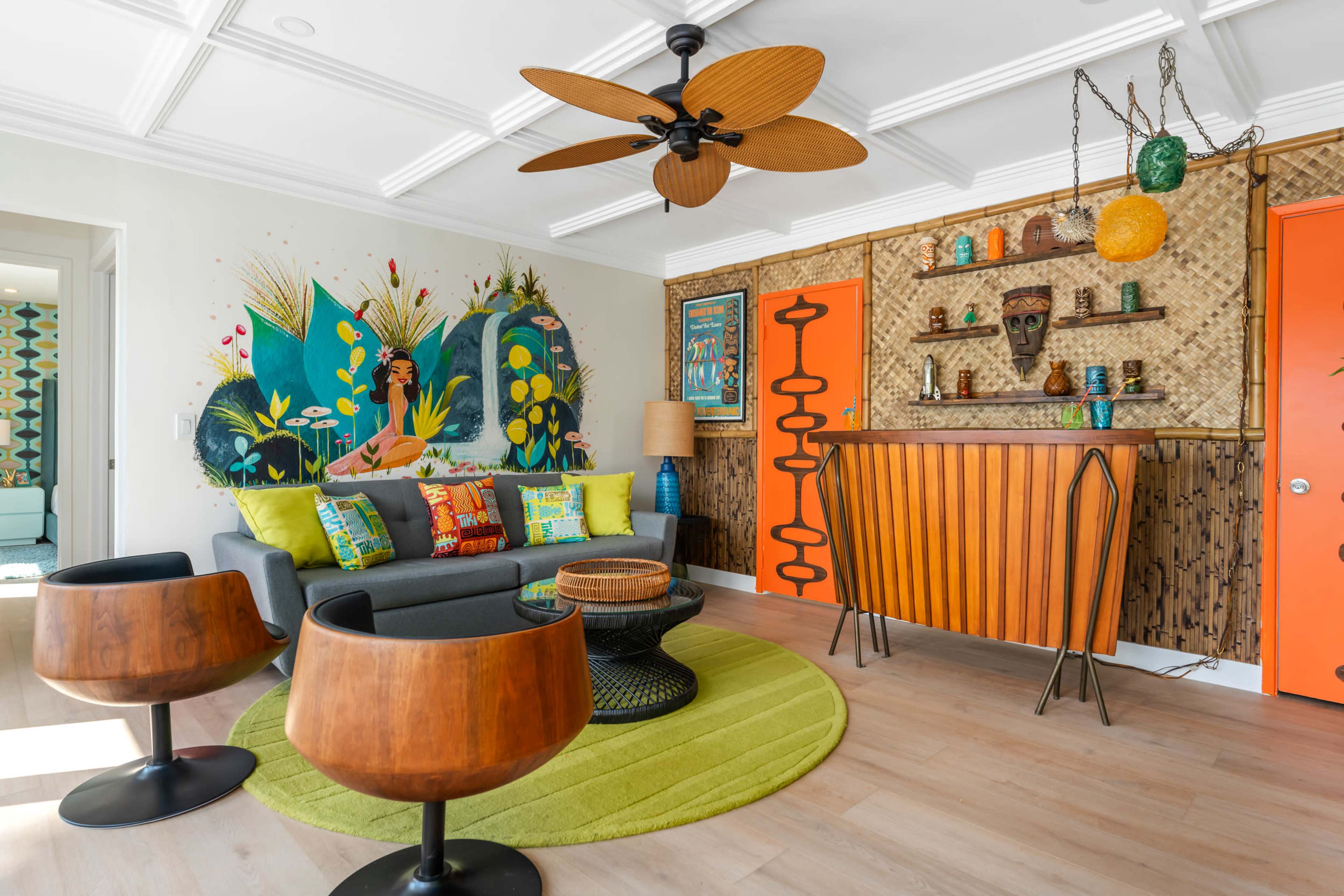 The living room features a colorful mural, a modern bar area with vibrant decorations, a round green rug, and wooden accent furniture.