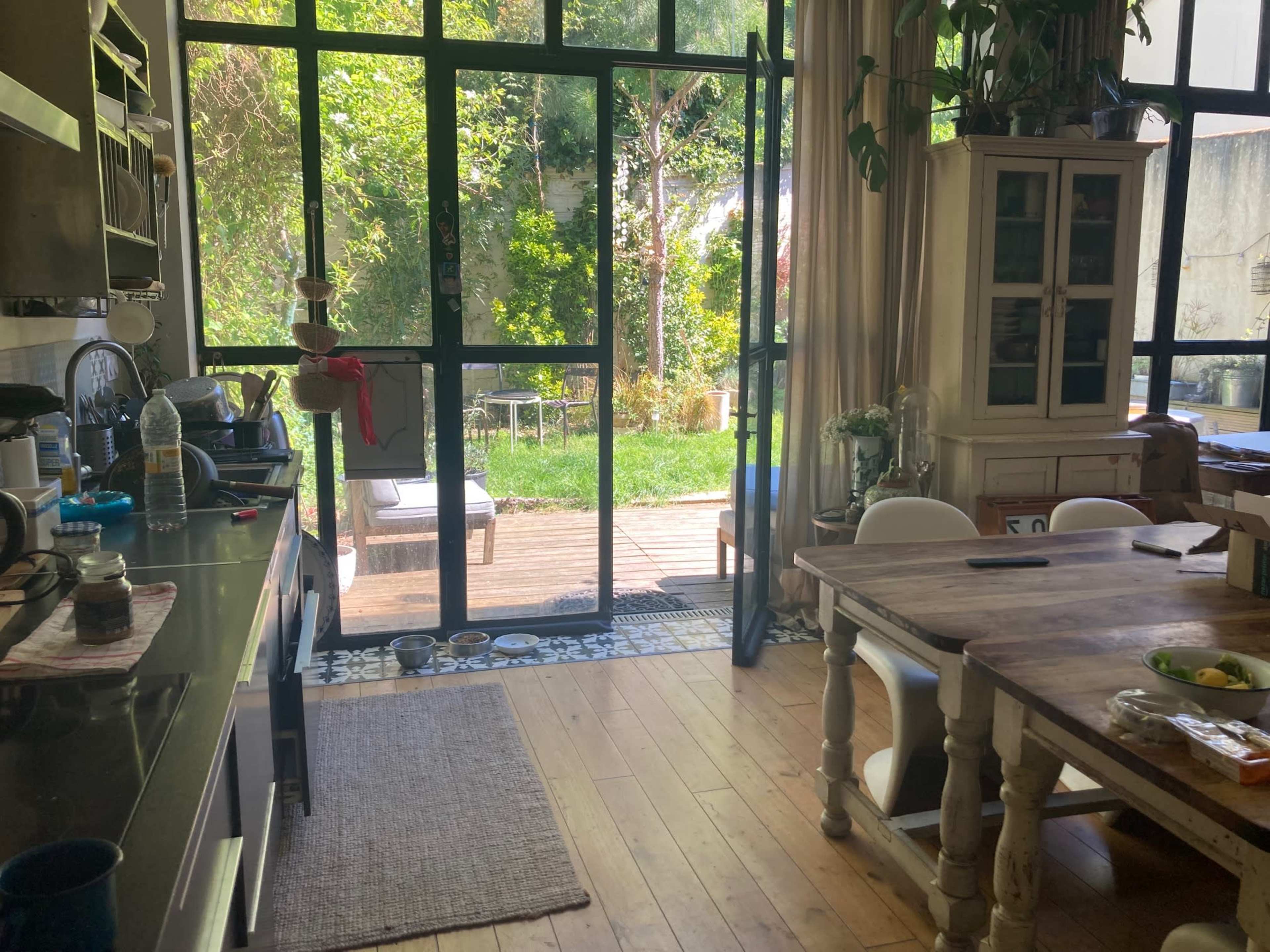 A spacious kitchen opens up to a green backyard through large glass doors, featuring wooden flooring and a rustic dining table.