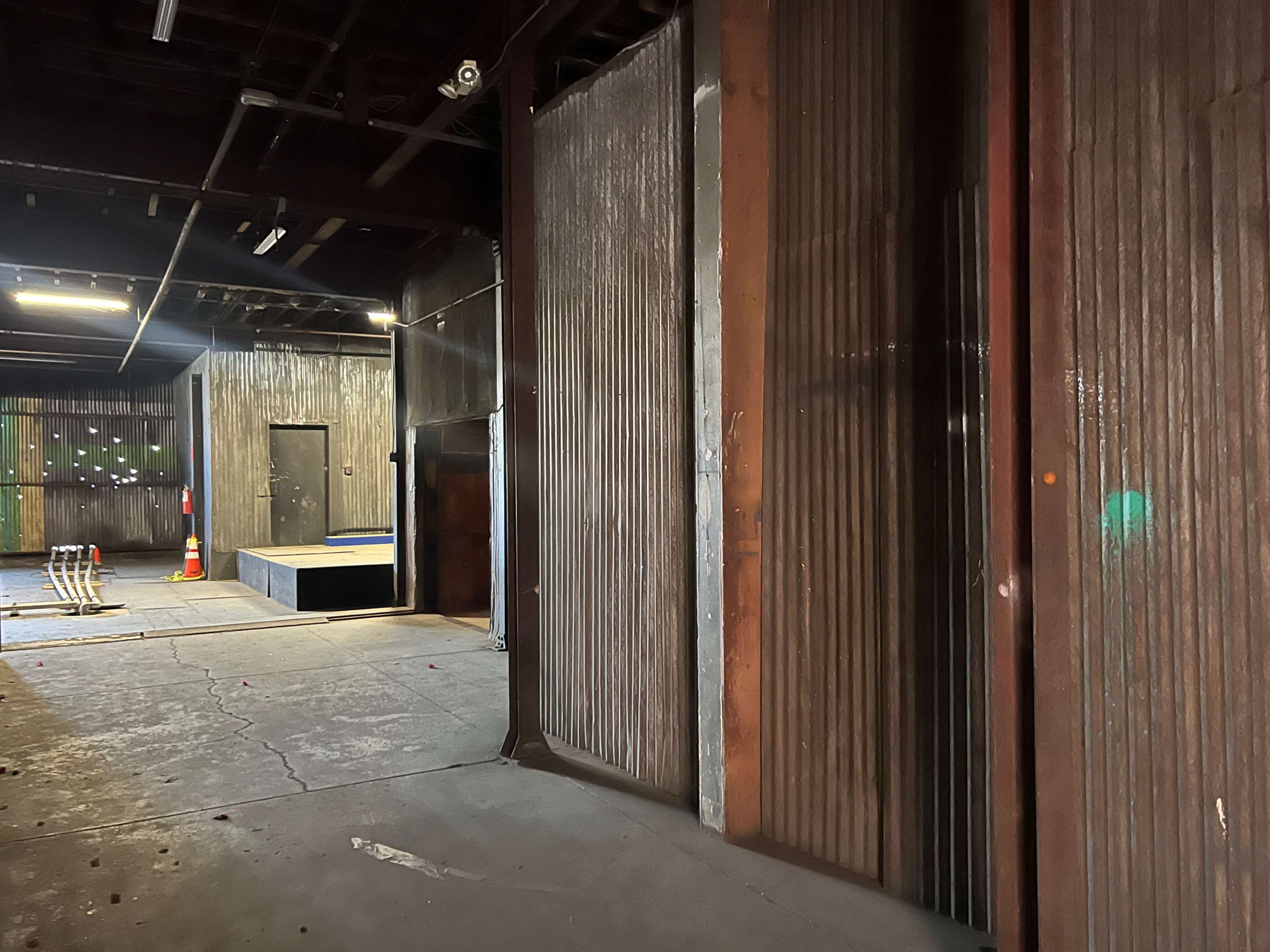 An industrial space features corrugated metal walls and a raised platform in the background, illuminated by overhead lights.