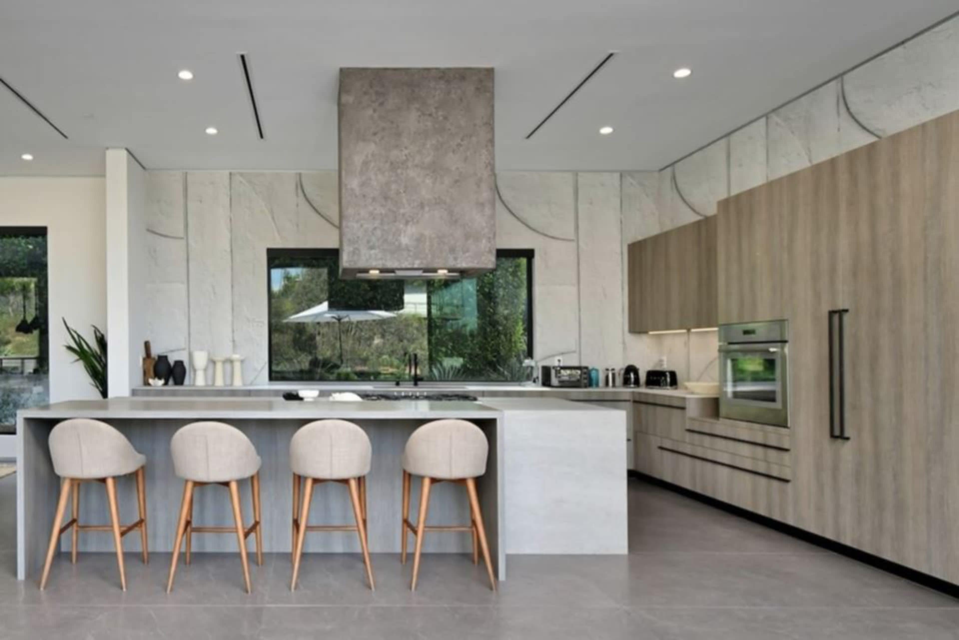 The image shows a modern kitchen with a large island, four stools, sleek cabinetry, and large windows.