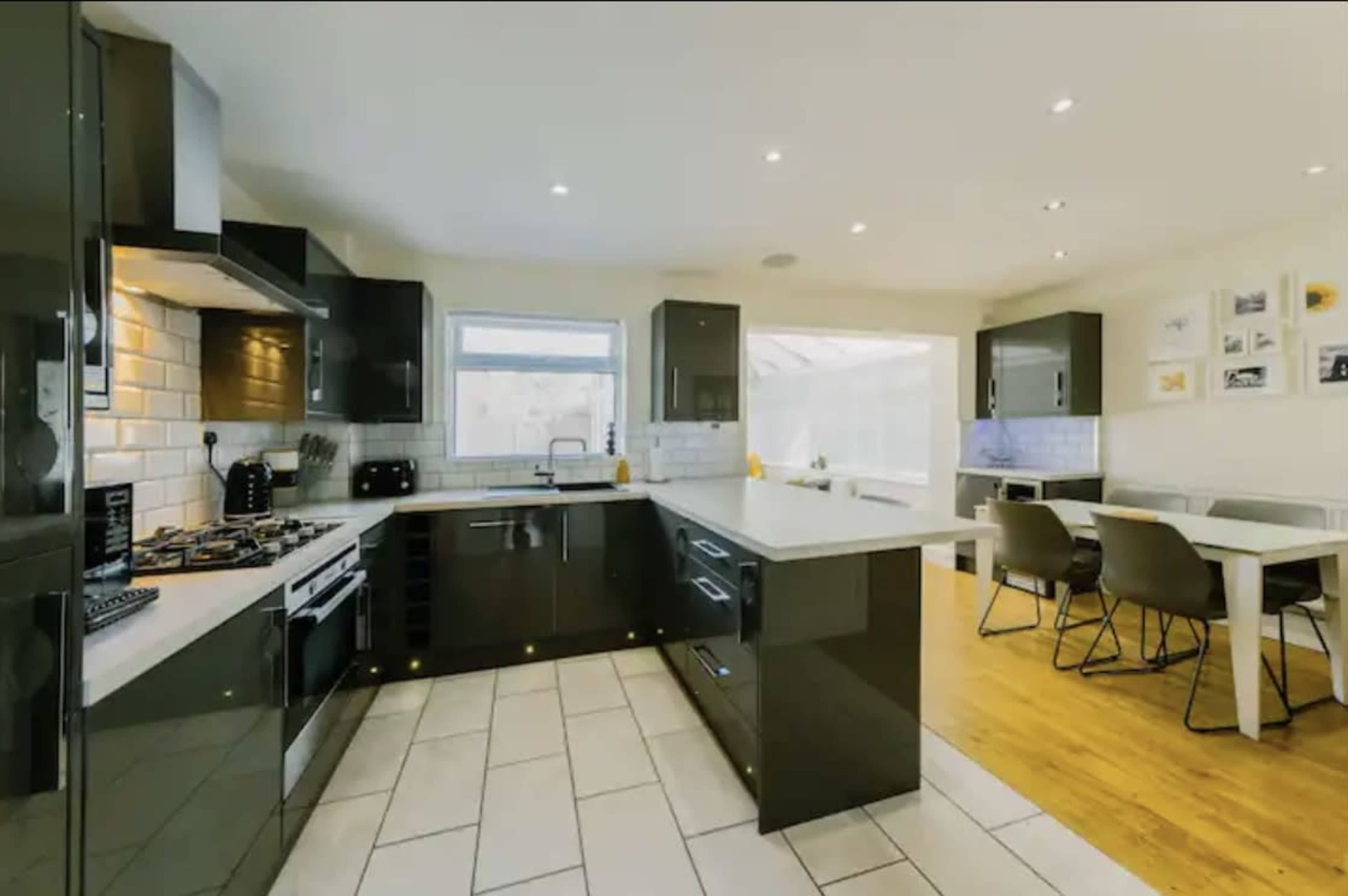 A modern kitchen featuring black cabinetry, white countertops, and an adjoining dining area with a wooden floor.