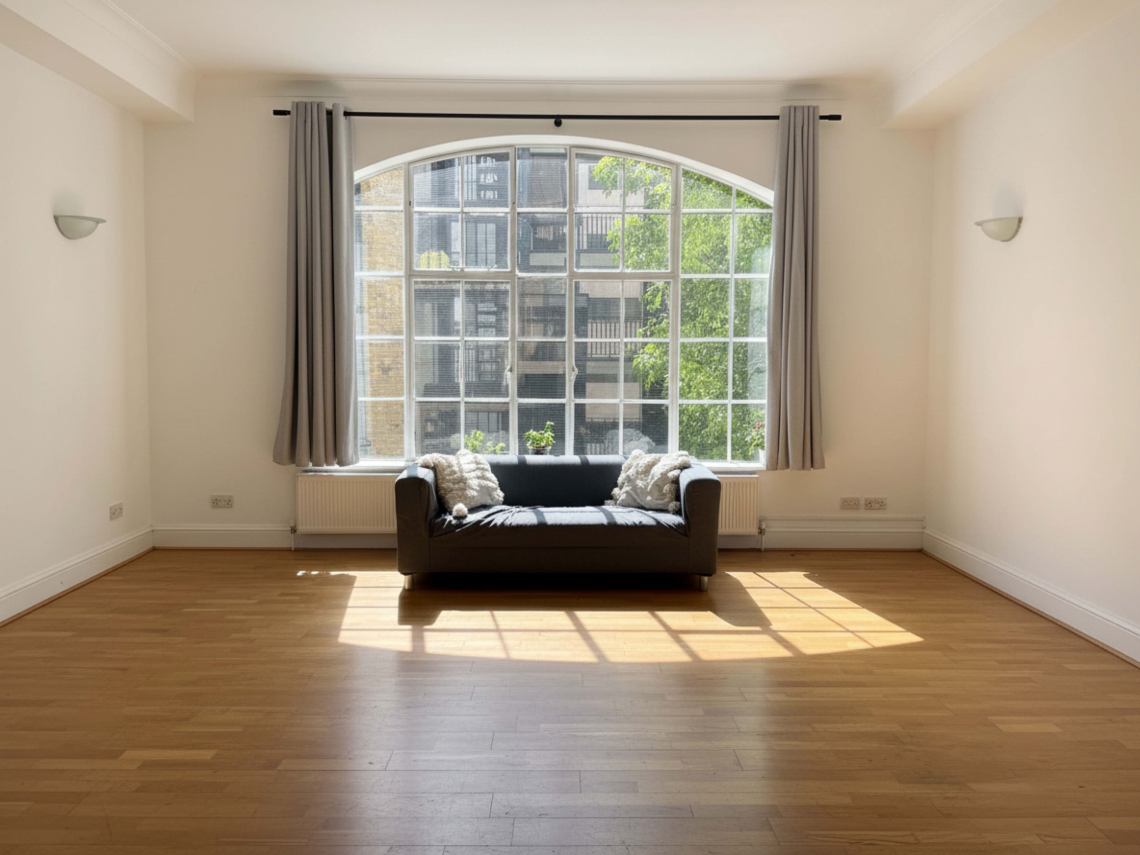 The room features a large arched window with natural light spilling onto a couch, illuminating the wooden floor.