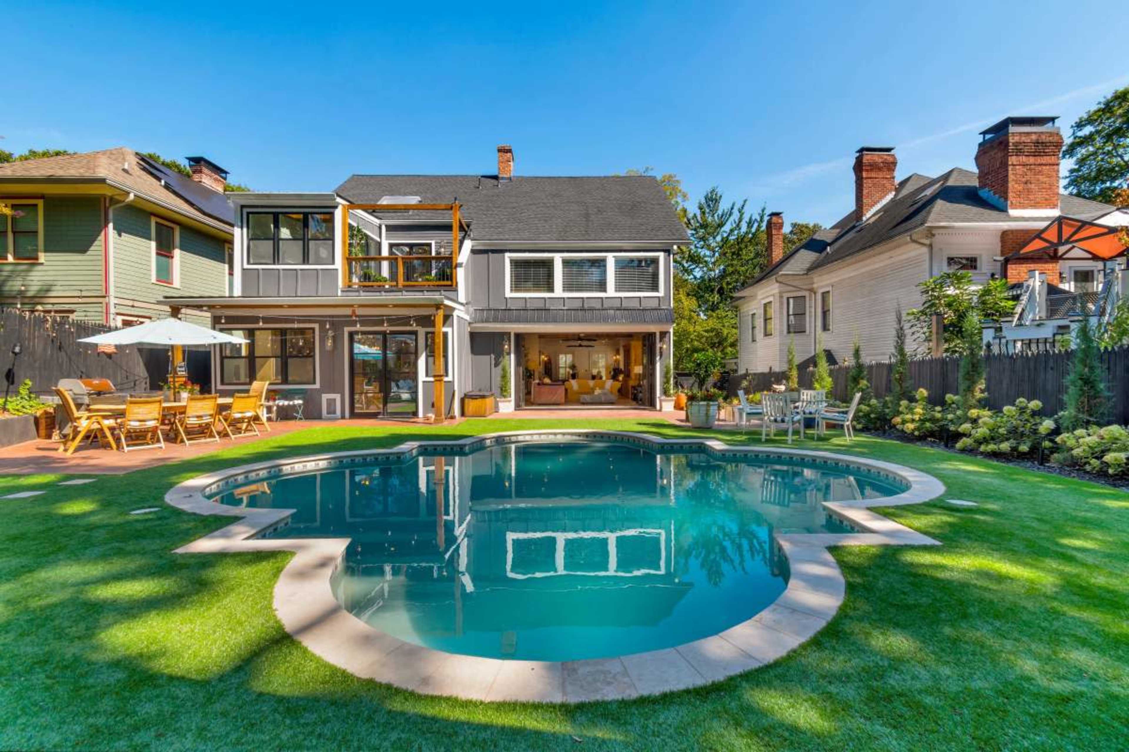 The image shows a two-story house with a patio and swimming pool surrounded by a landscaped lawn and several outdoor seating areas.