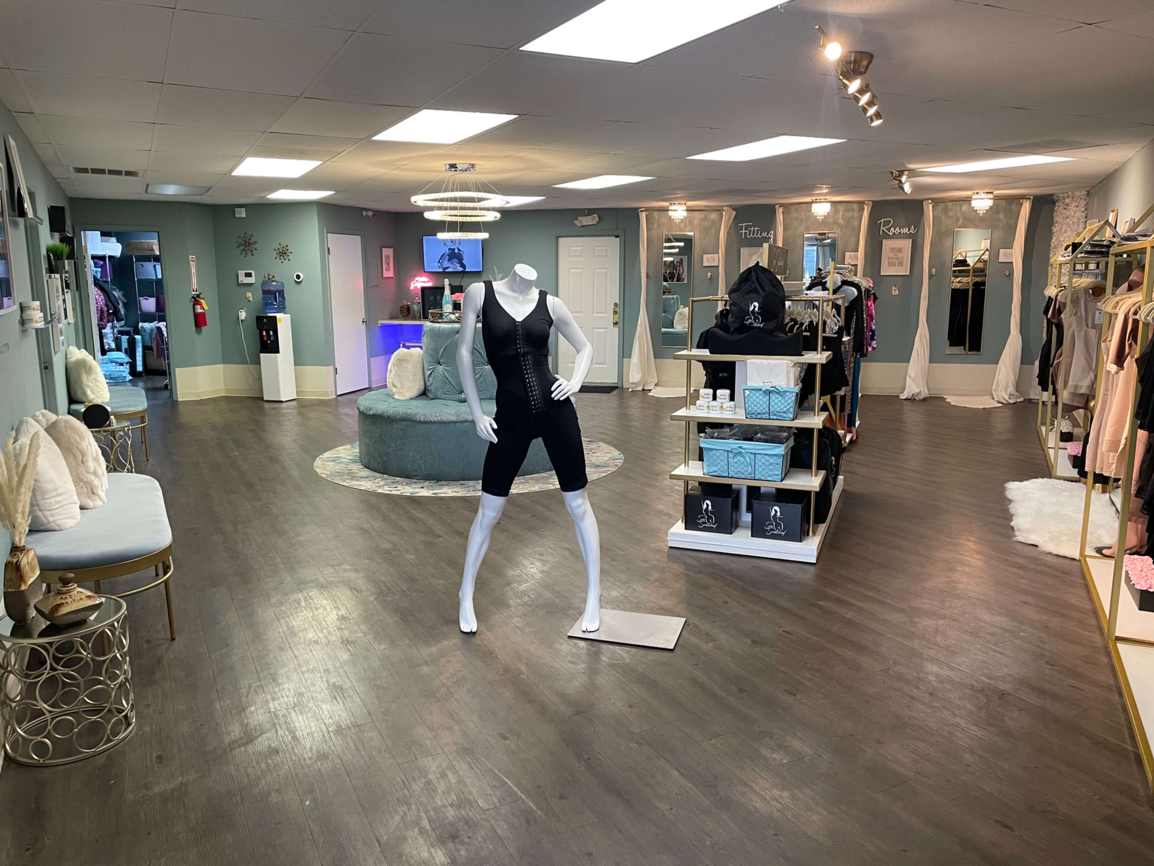 An interior of a boutique featuring a mannequin dressed in activewear, surrounded by clothing racks and displays on wooden flooring.
