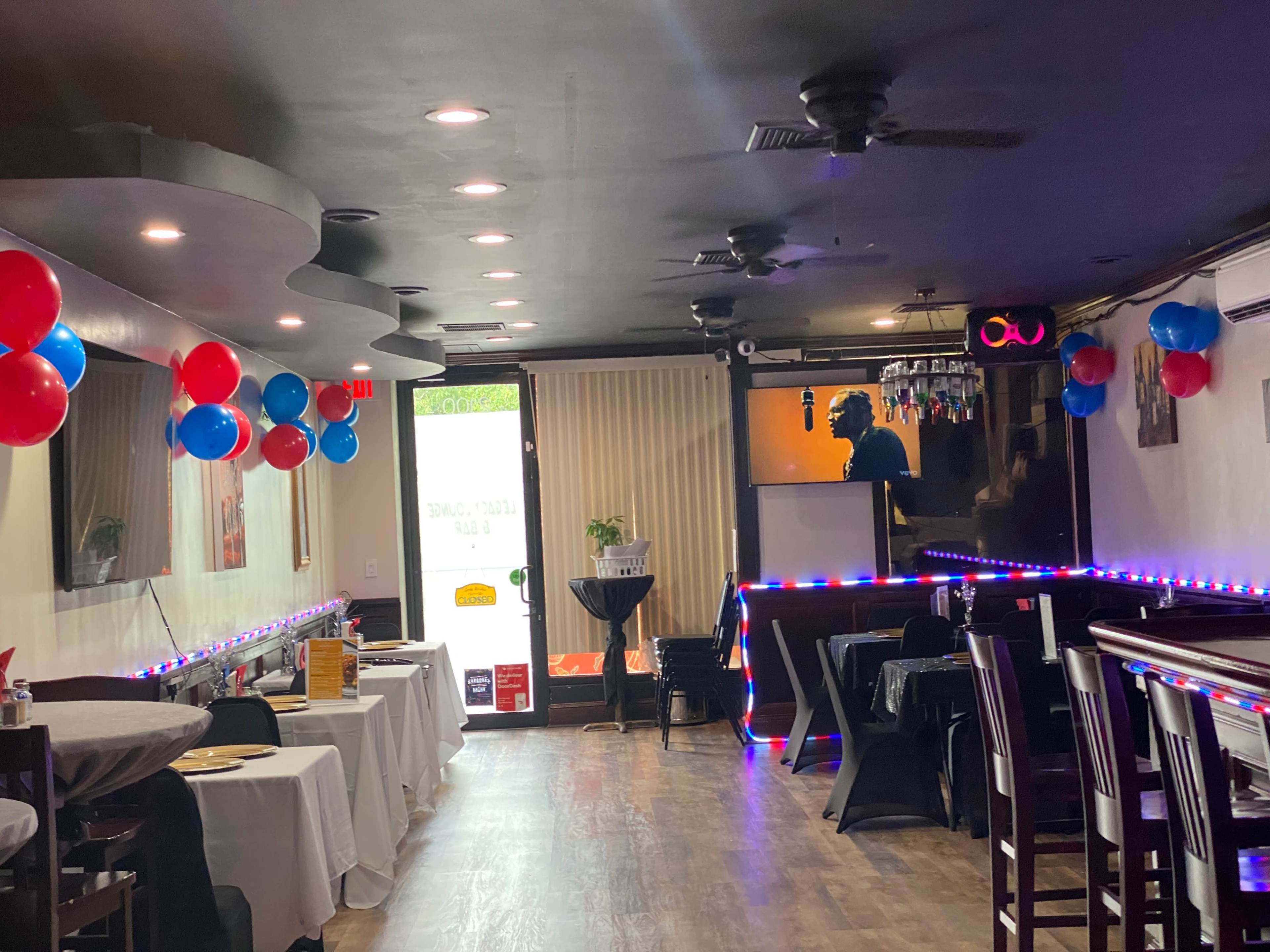 The interior of a restaurant features tables covered with white tablecloths, decorations in red and blue, and a stage area illuminated by soft lighting.