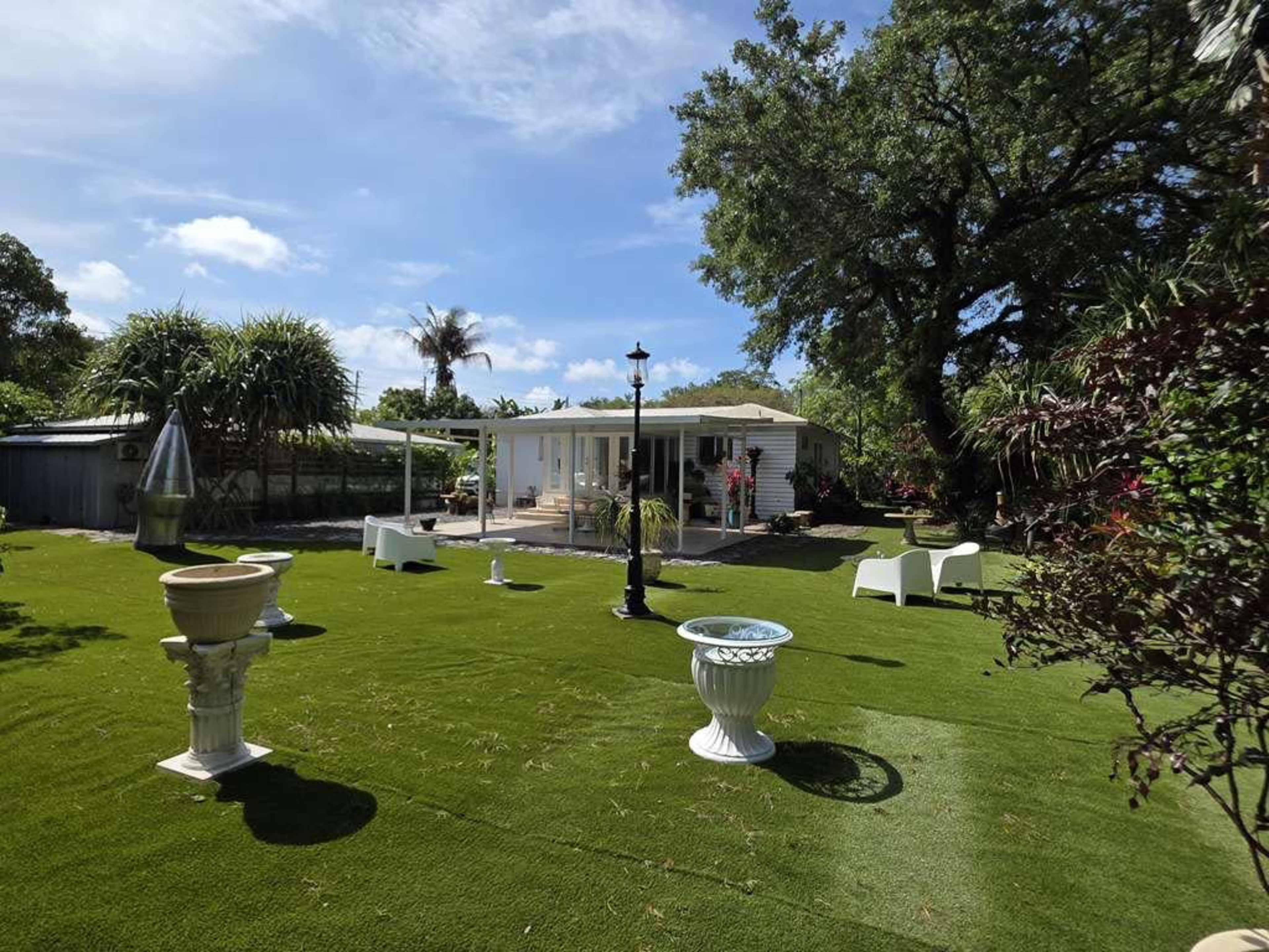 The image shows a well-maintained backyard with artificial grass, potted plants, and white outdoor furniture near a house.