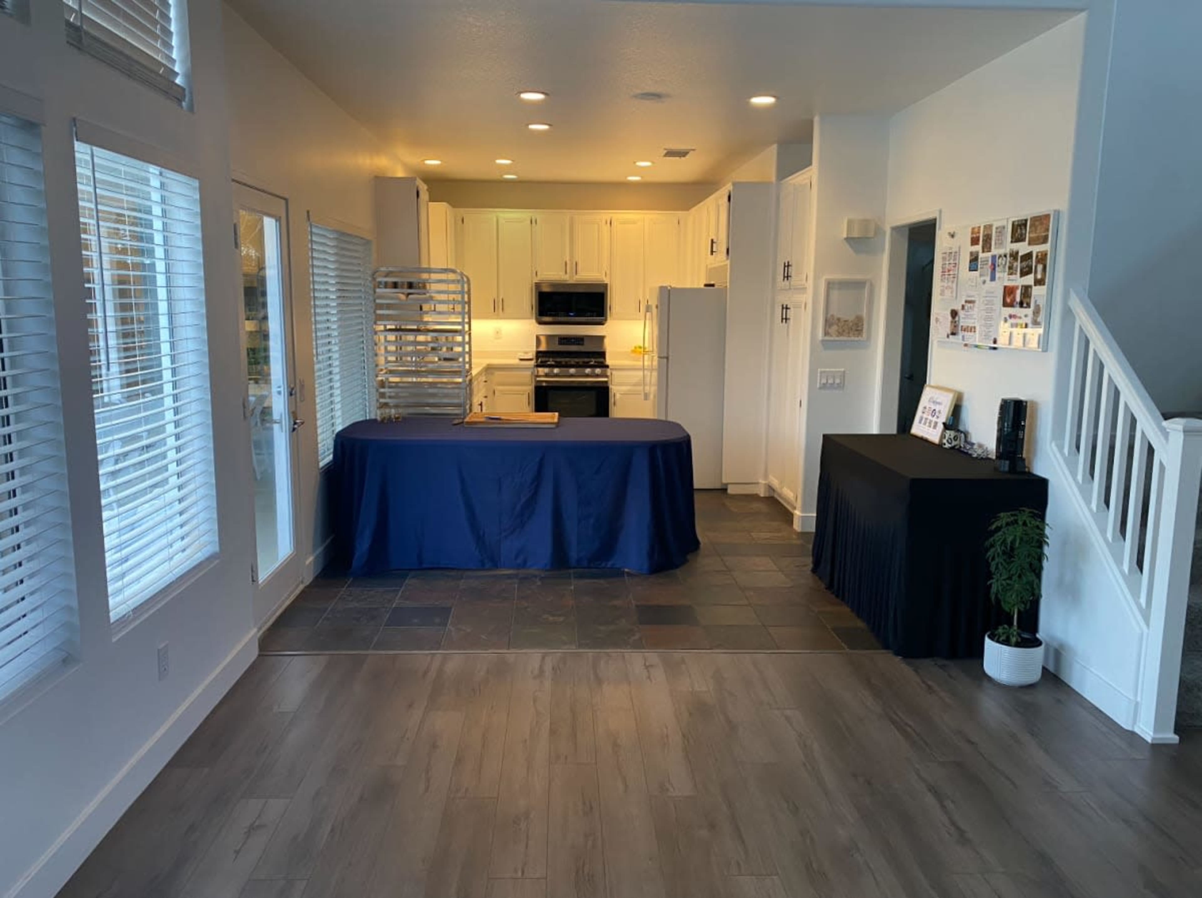 The image shows a modern, open kitchen area with a table covered in a blue cloth, positioned near a set of glass doors and a staircase.