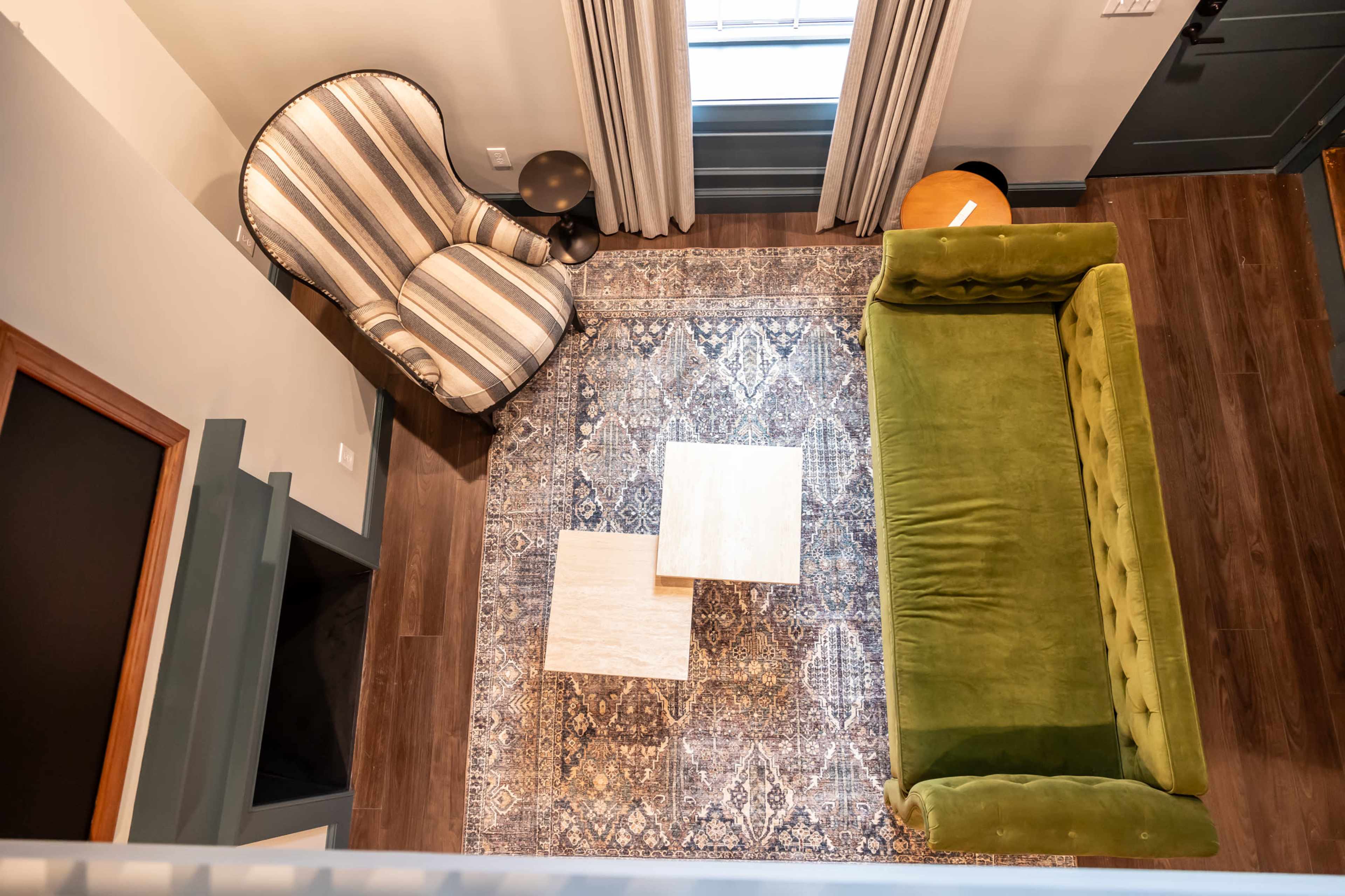 The image shows a living room from an overhead perspective, featuring a green sofa, two small side tables, a striped armchair, and a patterned area rug.