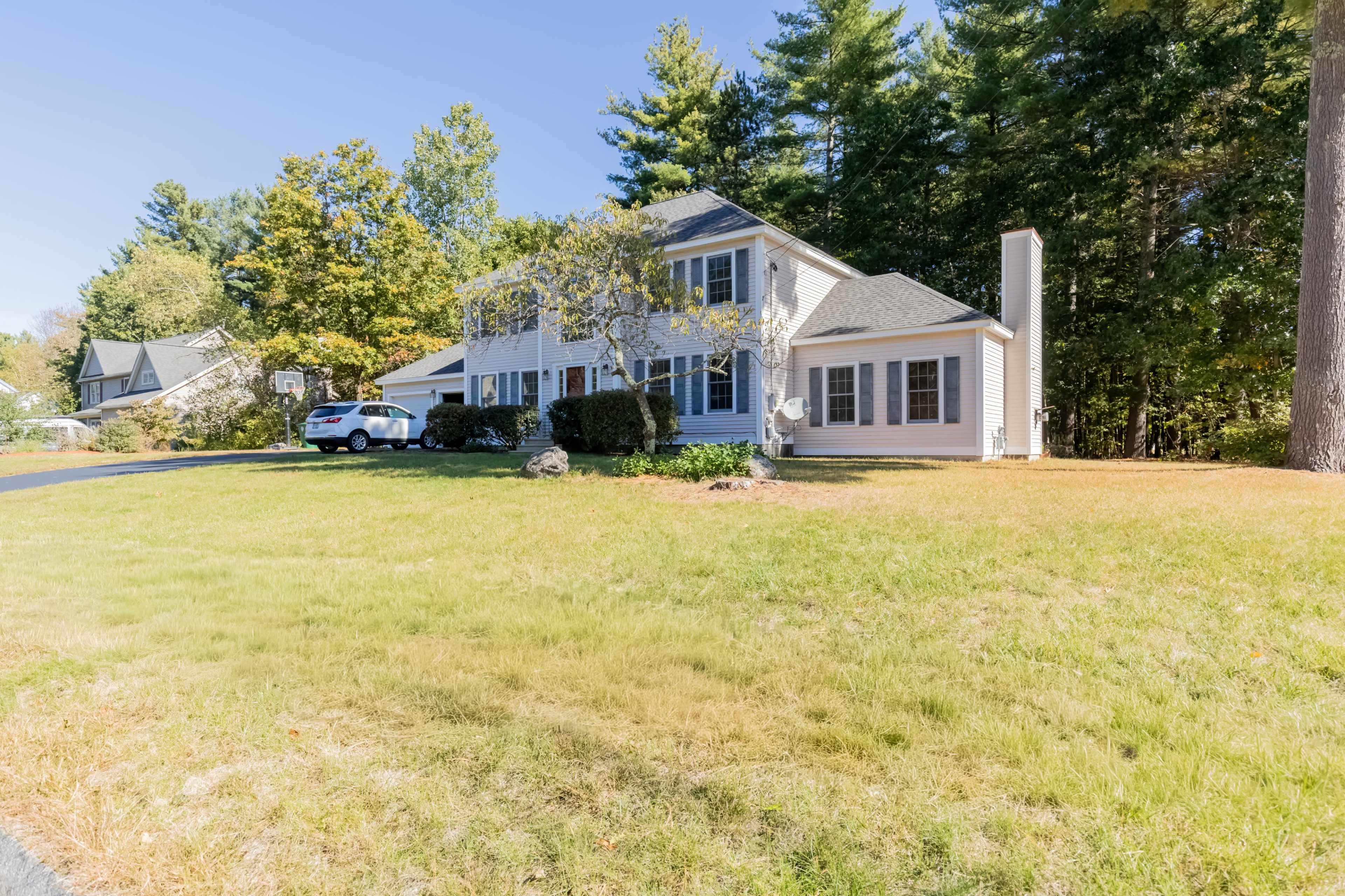 A two-story house with a light-colored exterior and a manicured lawn is situated on a tree-lined street.