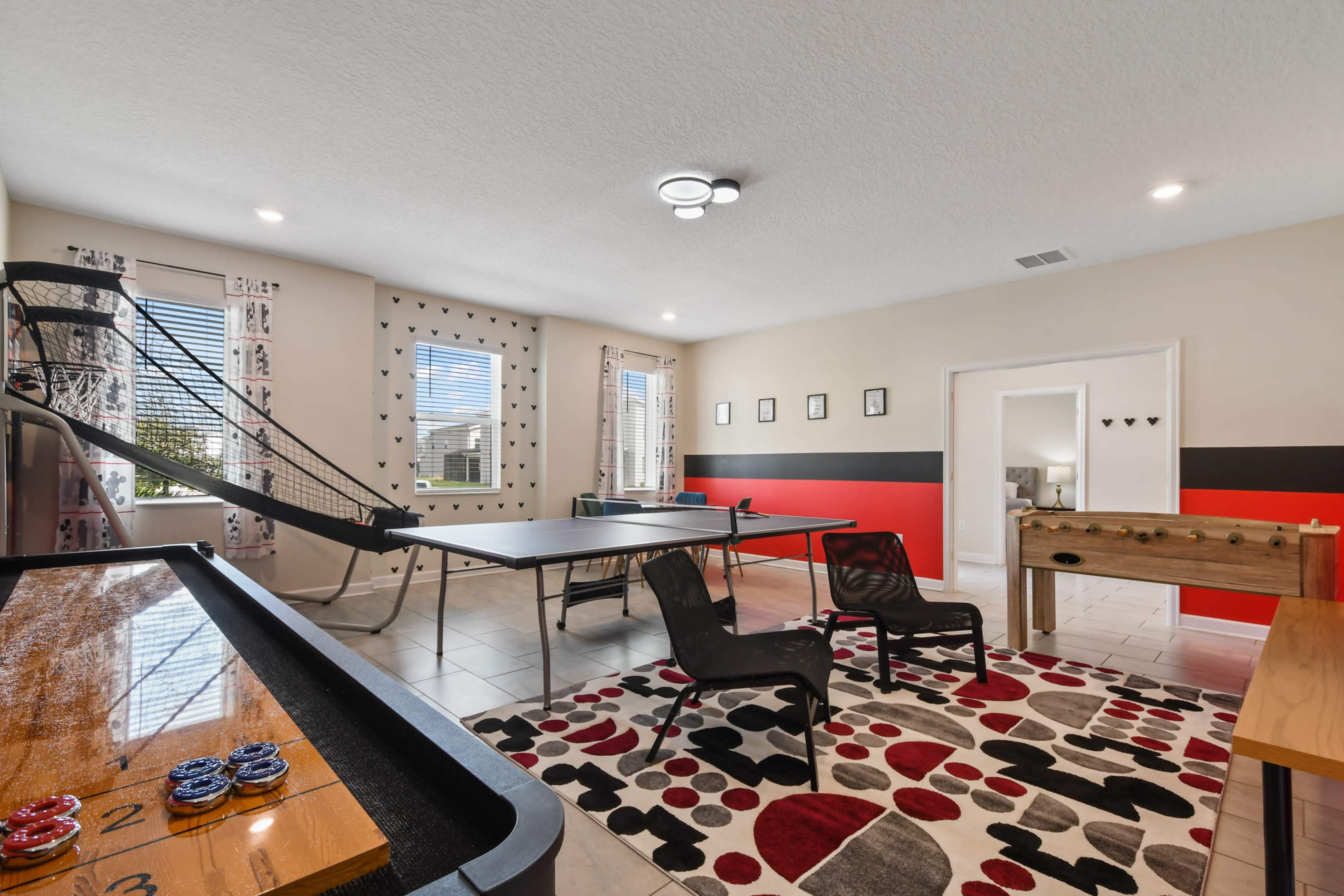 A recreational room with a pool table, a foosball table, a ping pong table, and a slide, all arranged on tiled flooring with colorful decor and seating.
