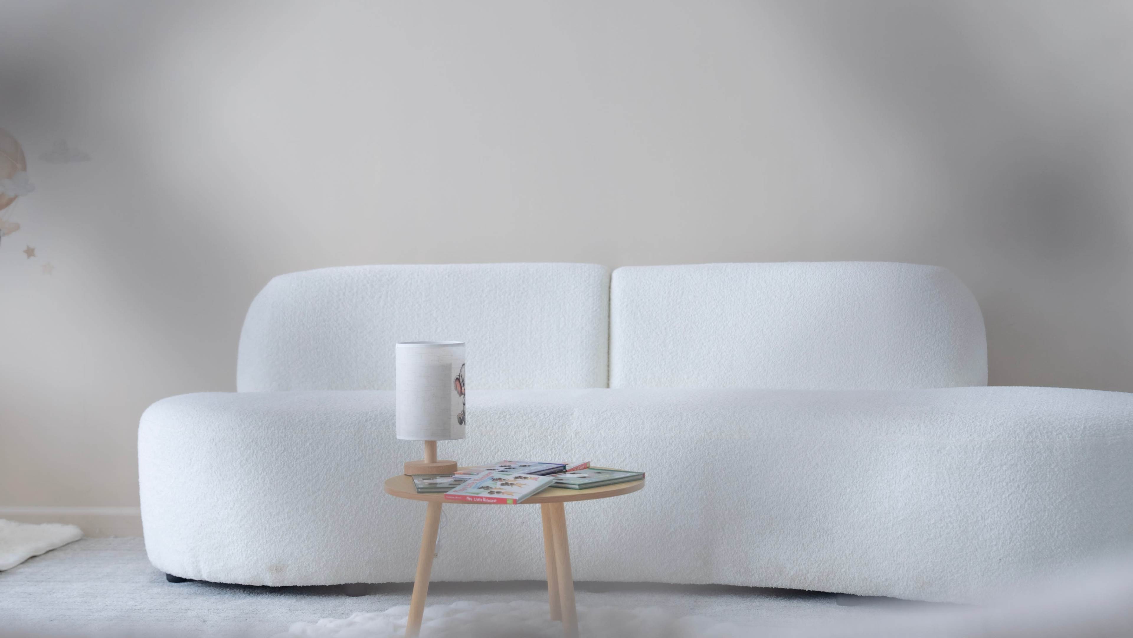 A white, plush sofa is positioned next to a small, light-colored wooden side table stacked with magazines.