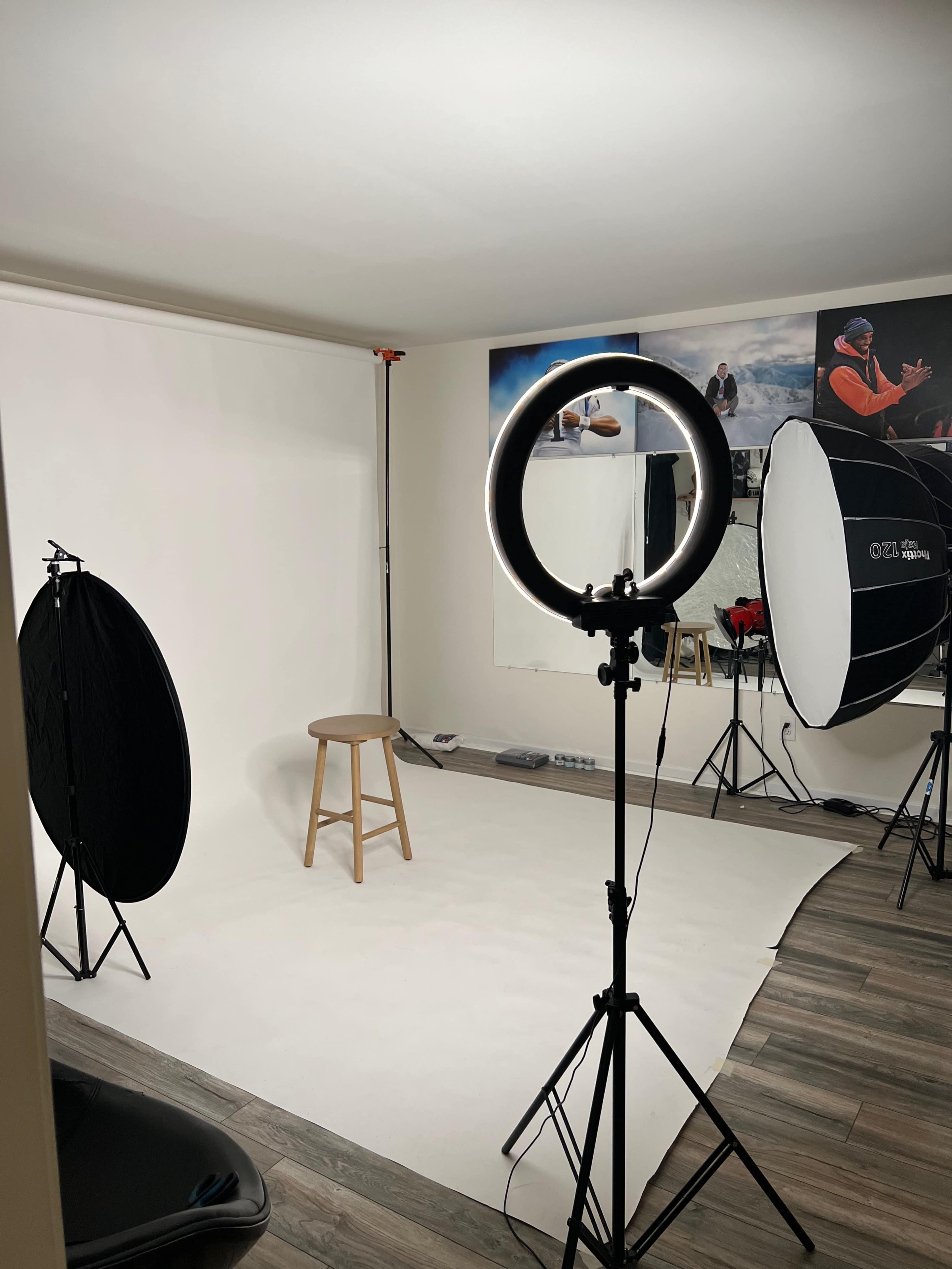 A photography studio setup with a stool on a white backdrop, illuminated by a ring light and softbox lamps.
