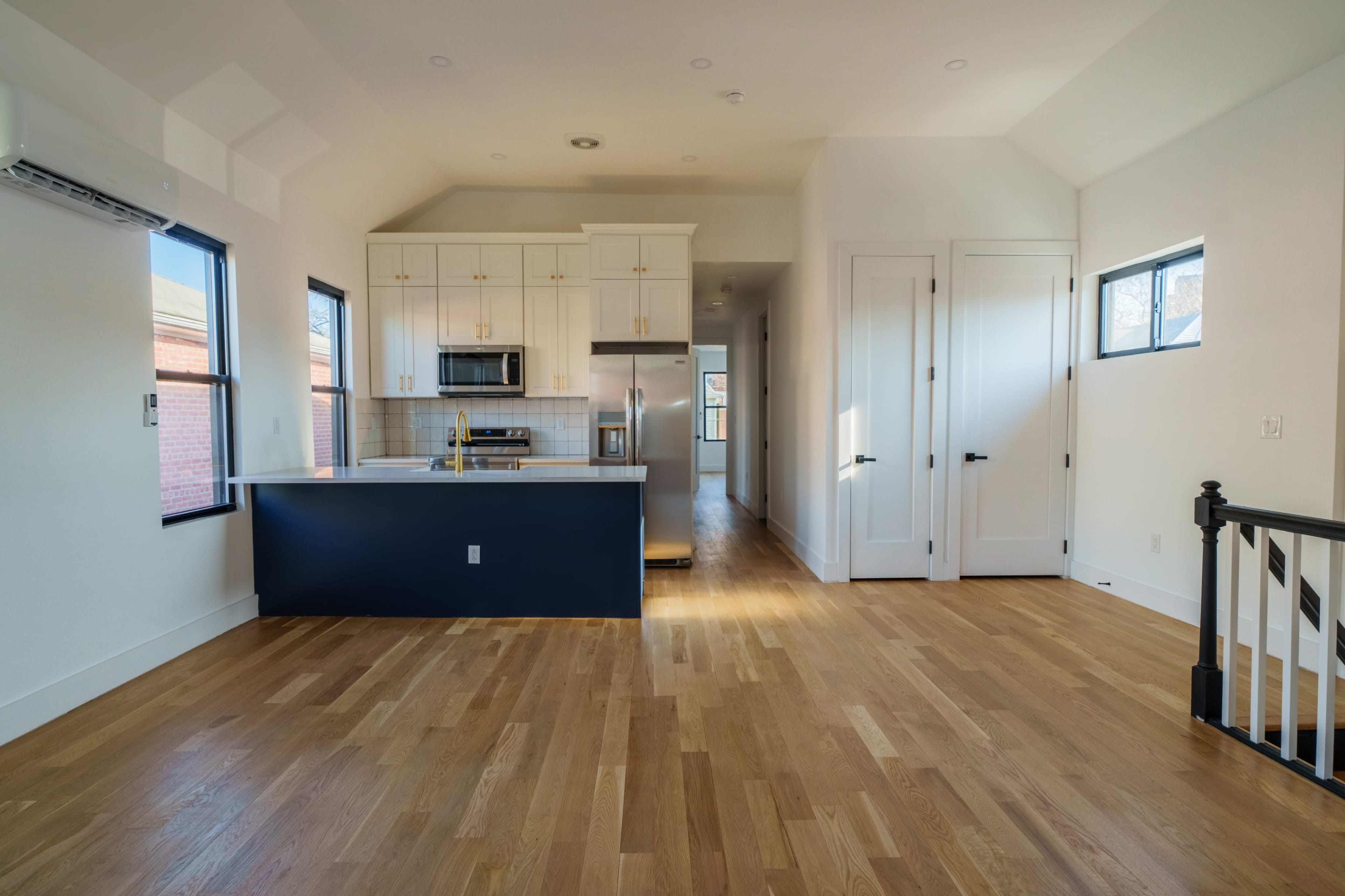 The image shows a modern, open-concept kitchen and living area with hardwood floors and large windows.