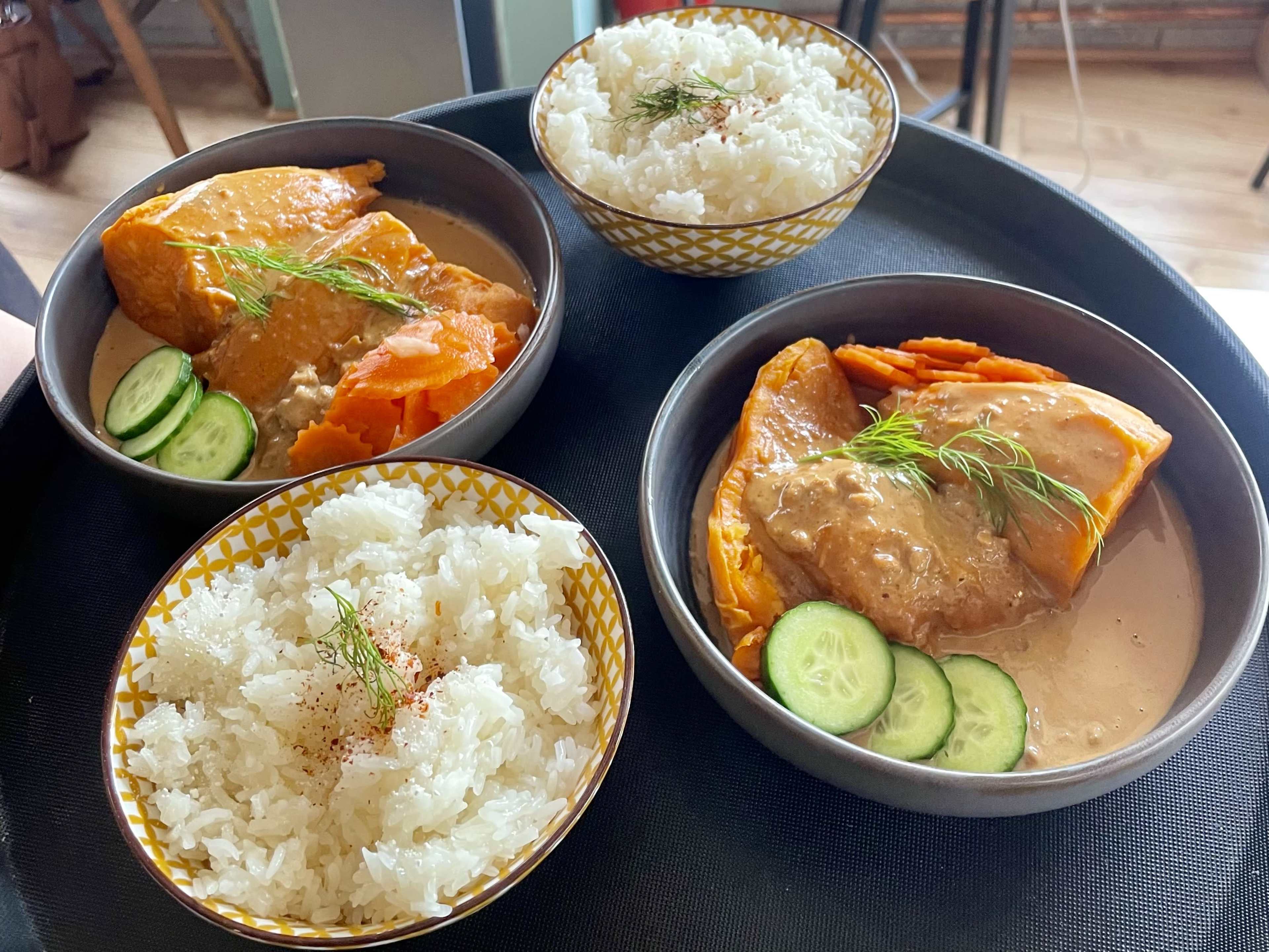 Three bowls of rice and salmon in a creamy sauce, garnished with cucumber slices and fresh herbs, are presented on a black tray.