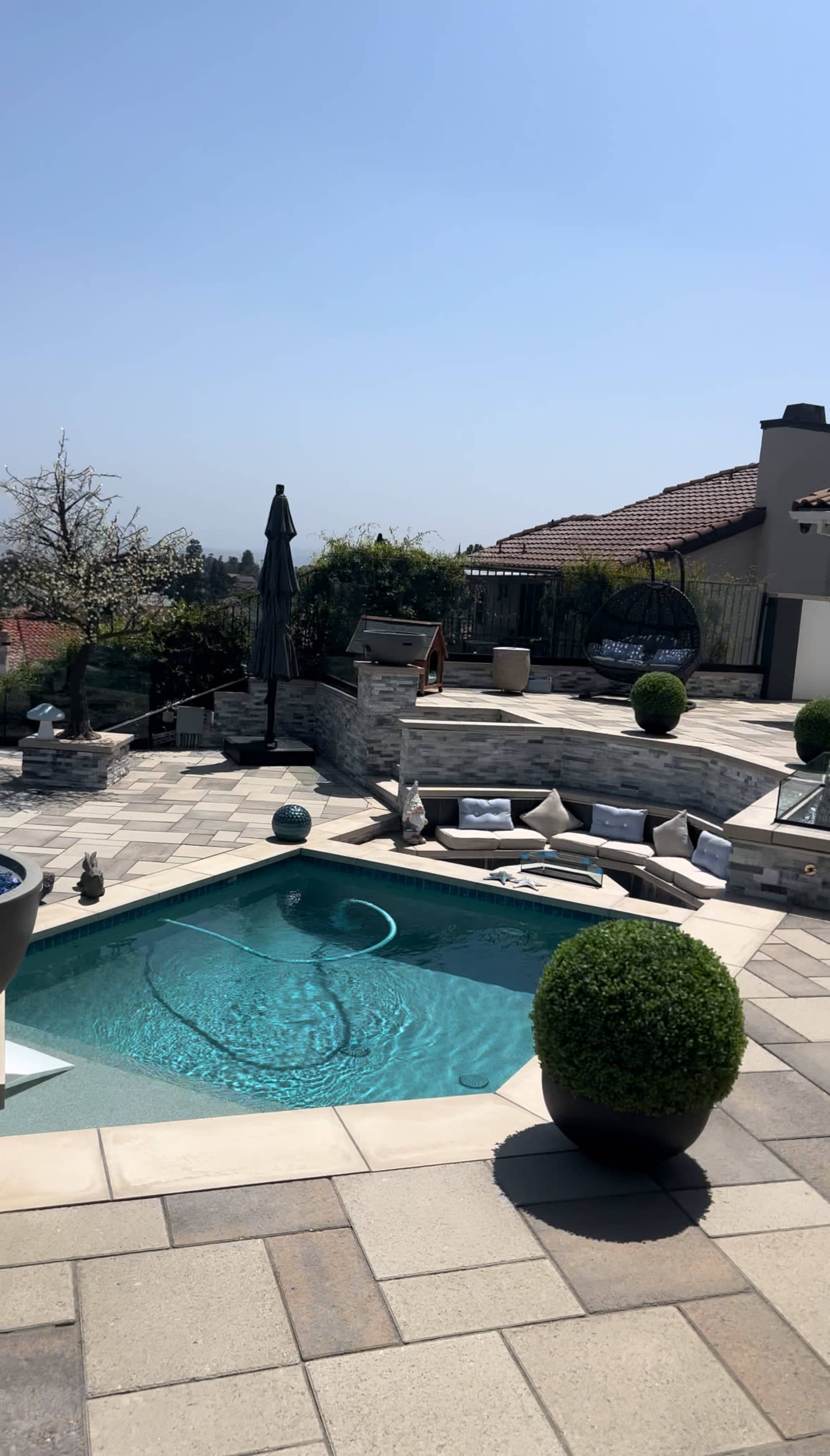A landscaped backyard with a shaped swimming pool, lounge area, and stone features under a clear sky.